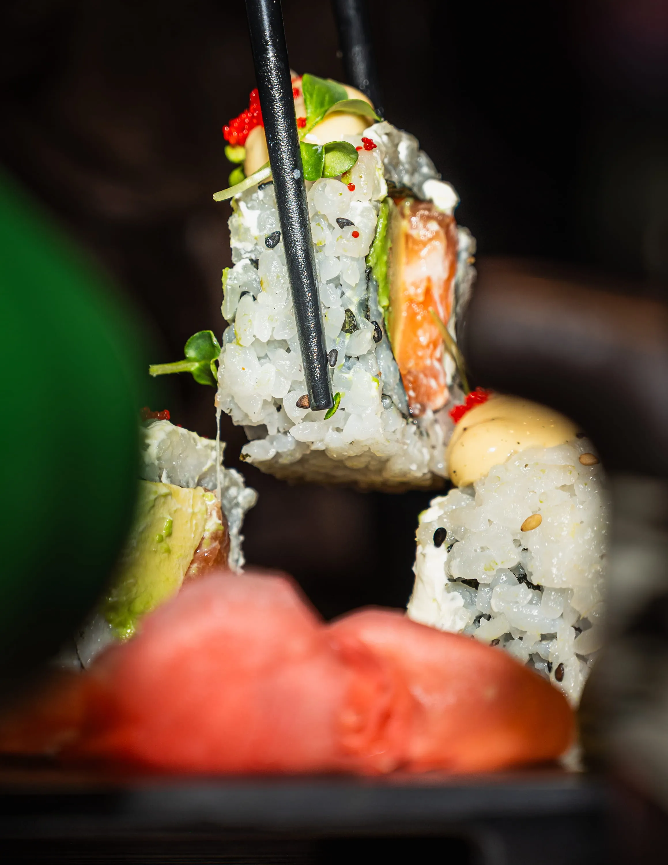 Nahaufnahme von Sushi-Rollen mit Reis, Avocado und rohem Lachs, eine Rolle wird mit Essstäbchen gehalten.