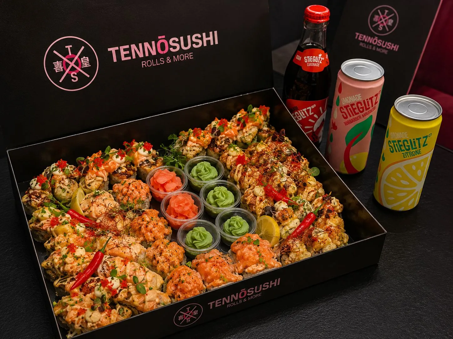 Große Sushi-Auswahl in Box mit Wasabi, Ingwer und drei Stieglitz Getränken in Dosen und Flasche.