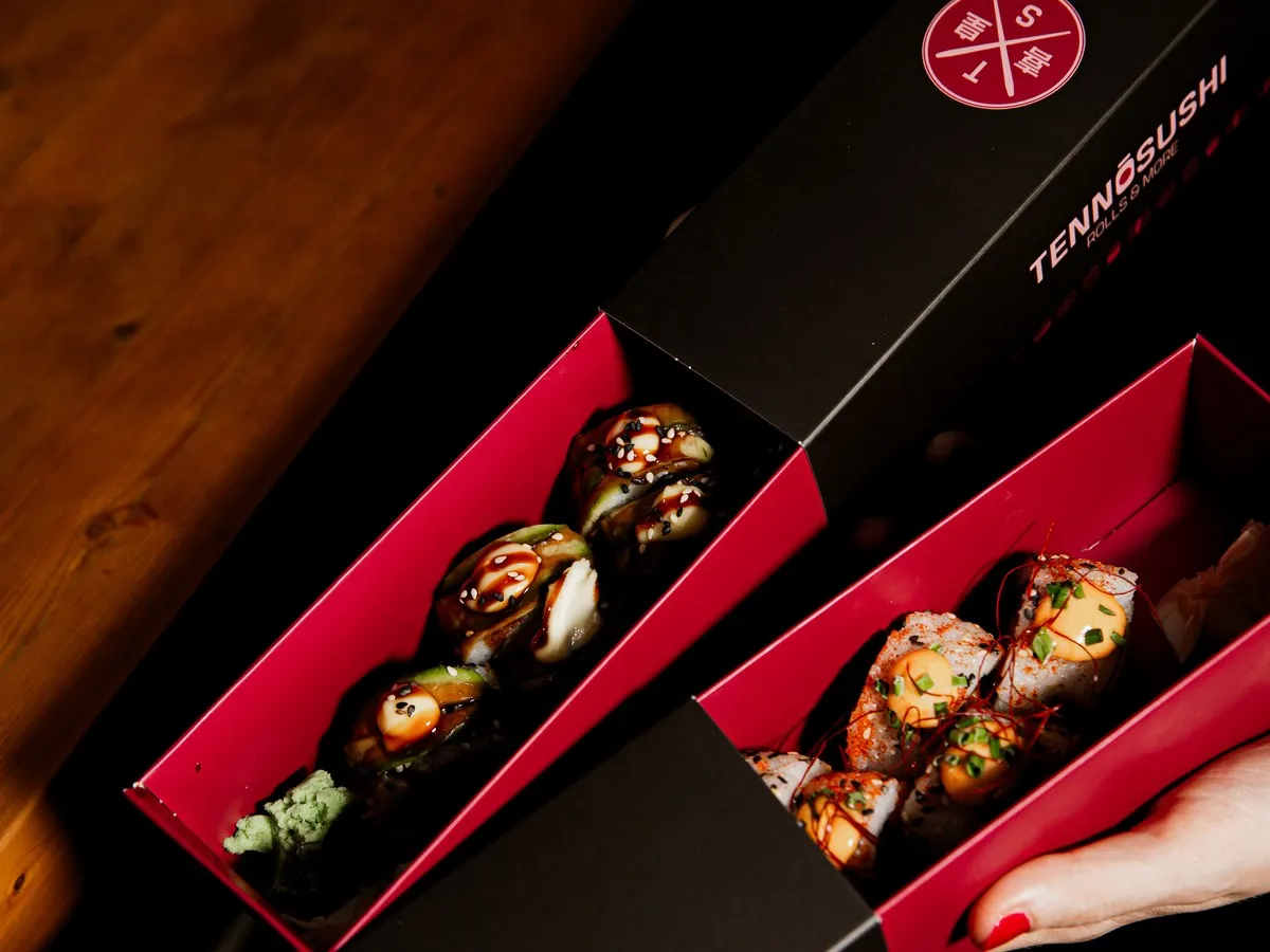 Zwei geöffnete Tenno Sushi Boxen mit Rolls, in der Hand gehalten.