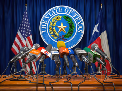 A table with press microphones in front of the State Seal of Texas