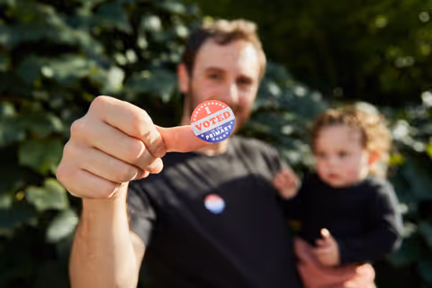 A dad holding his baby displaying a voted sticker