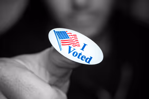 A black and white photo of a young man displaying his I Voted sticker