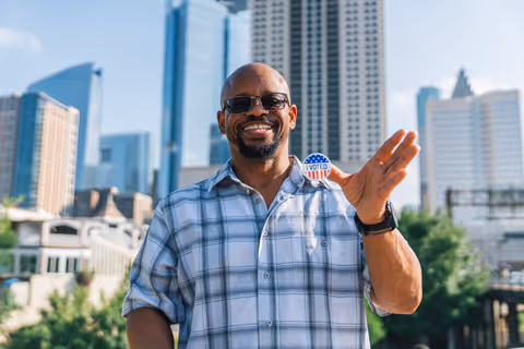 An adult man displaying his I Voted sticker in front of the Houston skyline