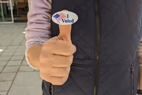 A young man displaying his I Voted sticker on his thumb