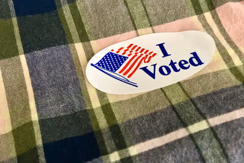 A close up photo of an I Voted sticker on a plaid shirt