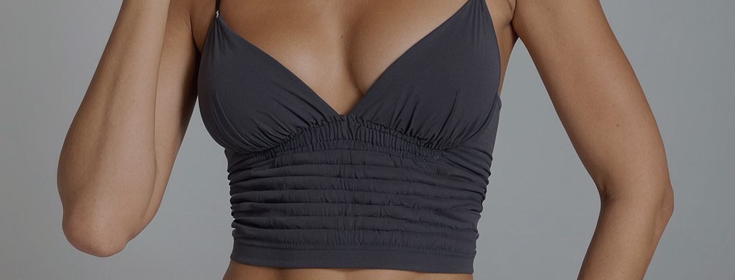 A model wearing a gray cropped top with a gathered design at the center and thin straps.