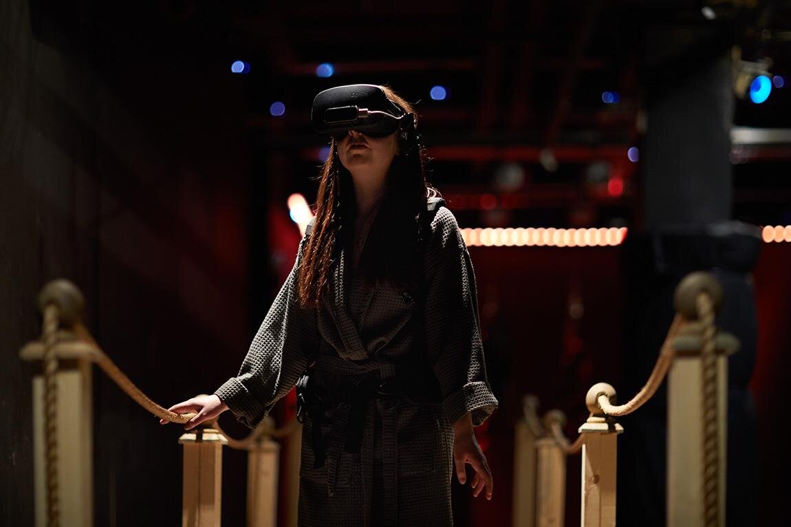 Person wearing a virtual reality headset walking cautiously while holding a rope handrail in a dimly lit environment.