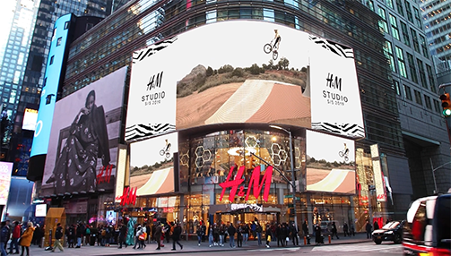 Crowded street view of H&M store with large digital screens showing a BMX rider performing a jump on a ramp.