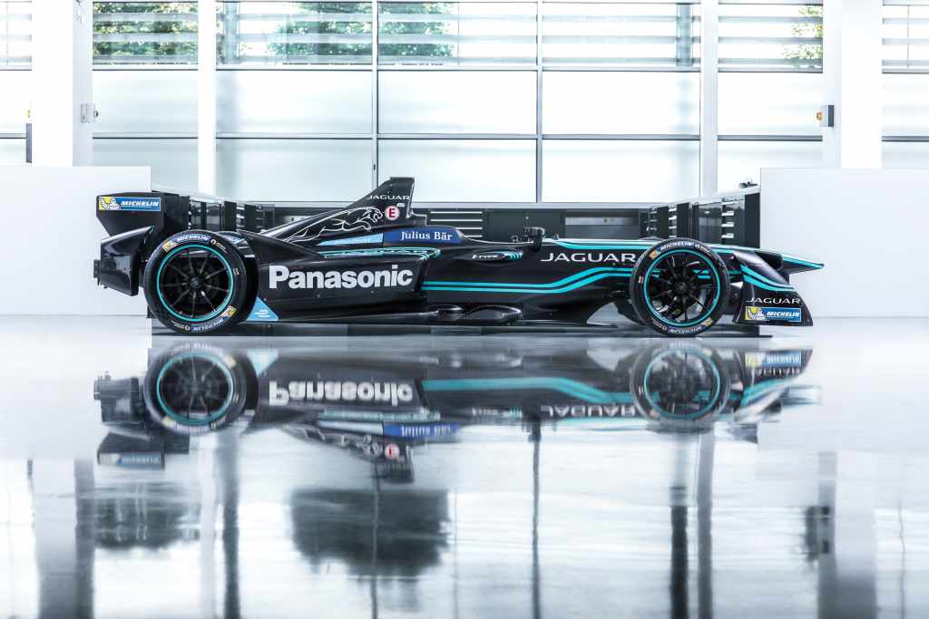 Side view of a sleek black Jaguar Panasonic racing car with blue accents, reflected on the polished floor.