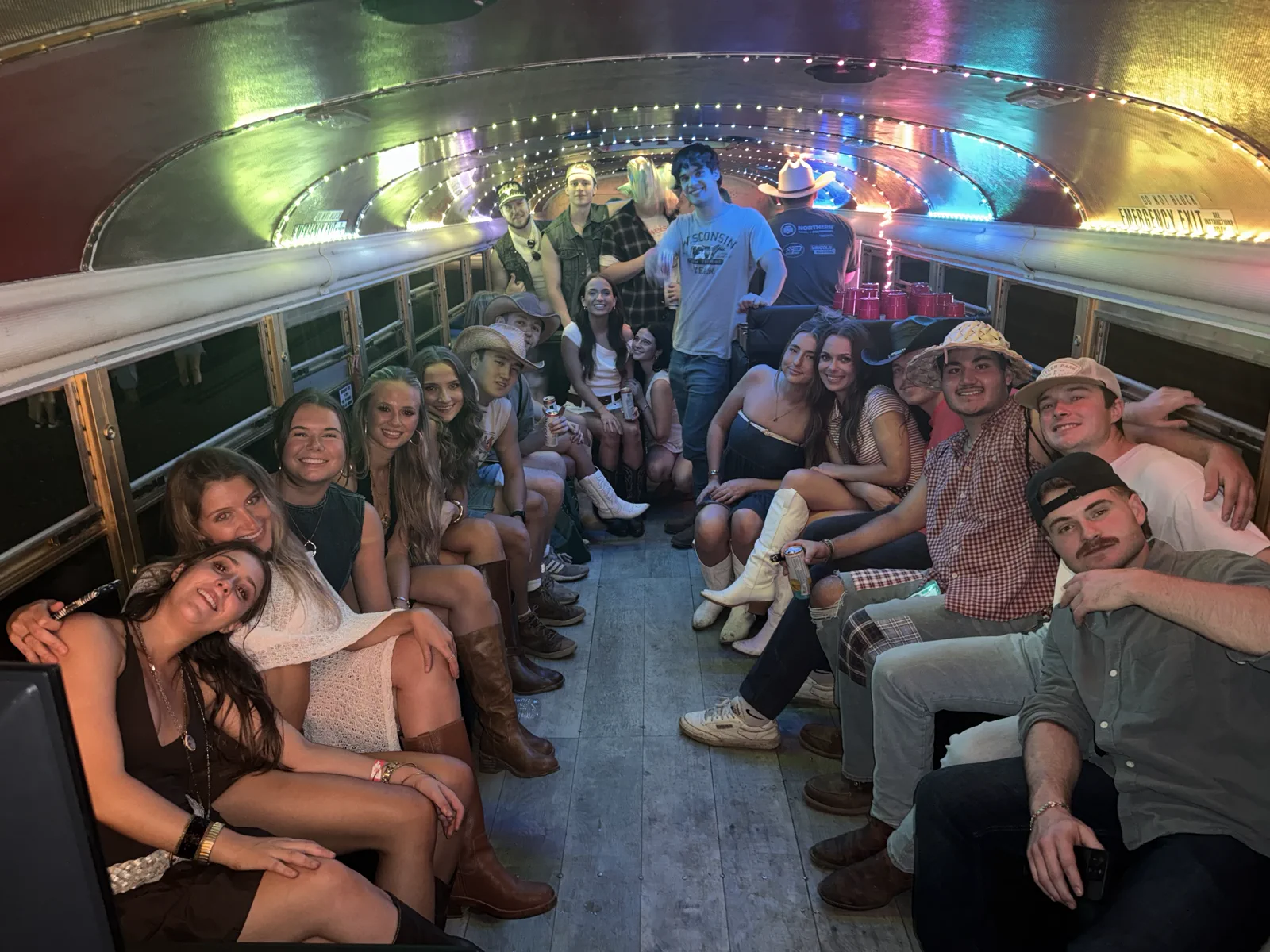 Group of young adults sitting and standing inside a decorated party bus with dynamic nightclub lights overhead.