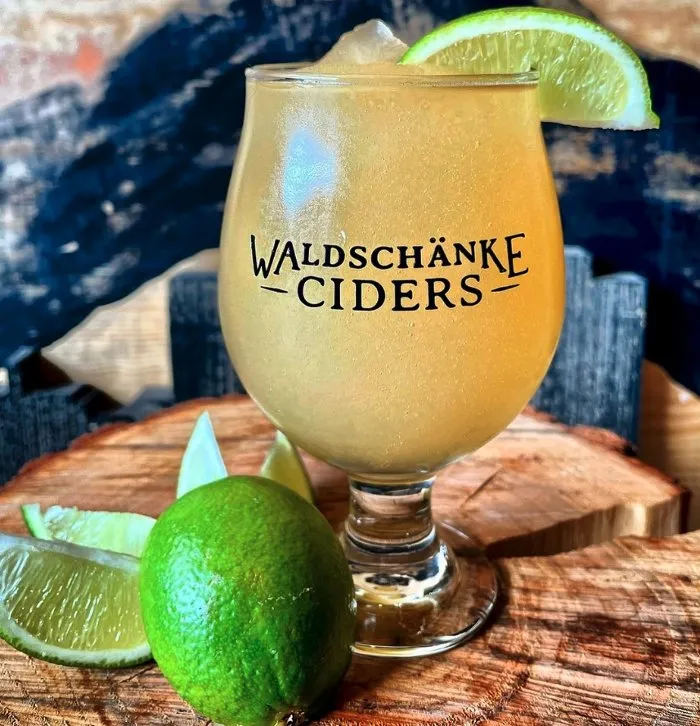 A glass of cider garnished with a slice of lime and a wedge of lime resting on the rim.