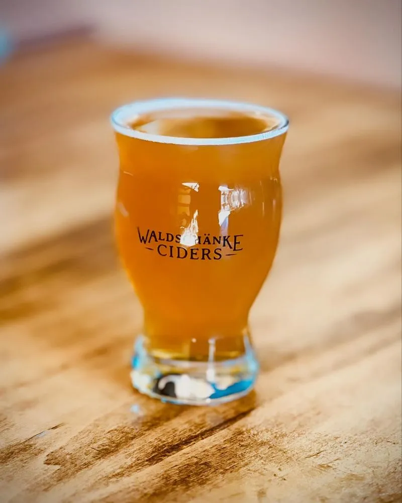 A glass of beer resting on a wooden table, showcasing its golden color and frothy head.