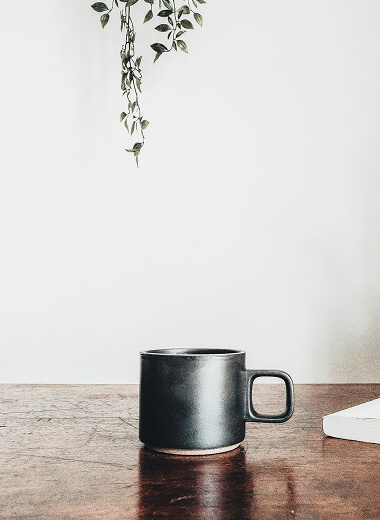 Black ceramic coffee mug on a wooden table with greenery, symbolizing calm, thoughtful financial planning.