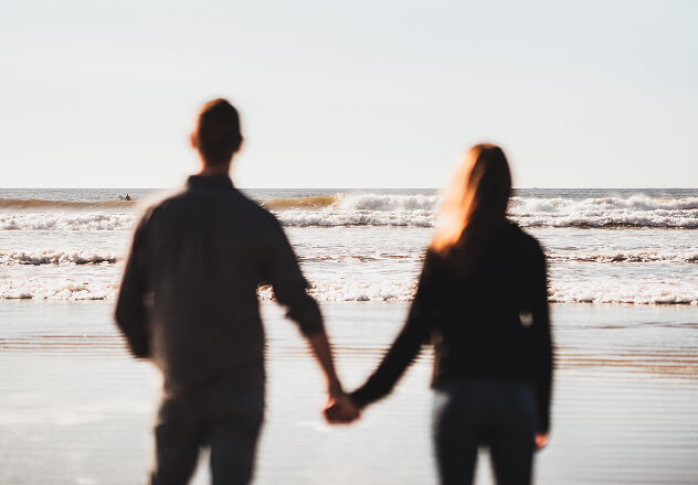 Couple holding hands while walking on a Maine beach, reflecting trusted partnership and values-aligned wealth management.