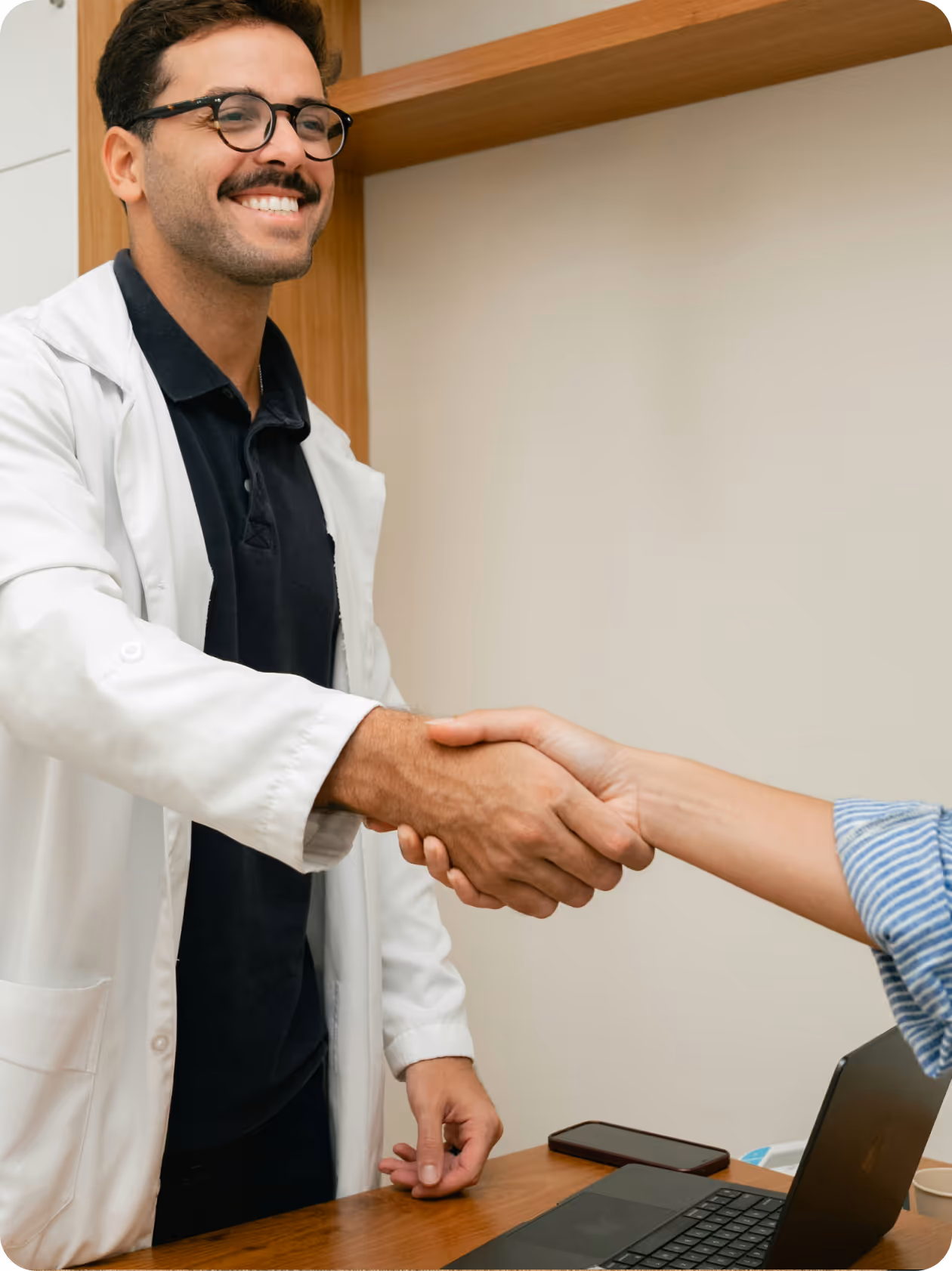 Male doctor with stethoscope smiling and reassuring a seated female patient in a clinic room.