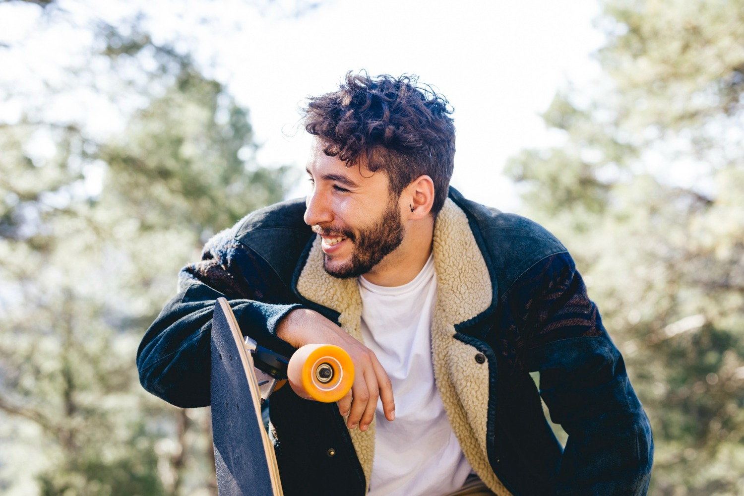 Smiling young man outdoors holding a skateboard, representing healthy lifestyle and positive recovery journey