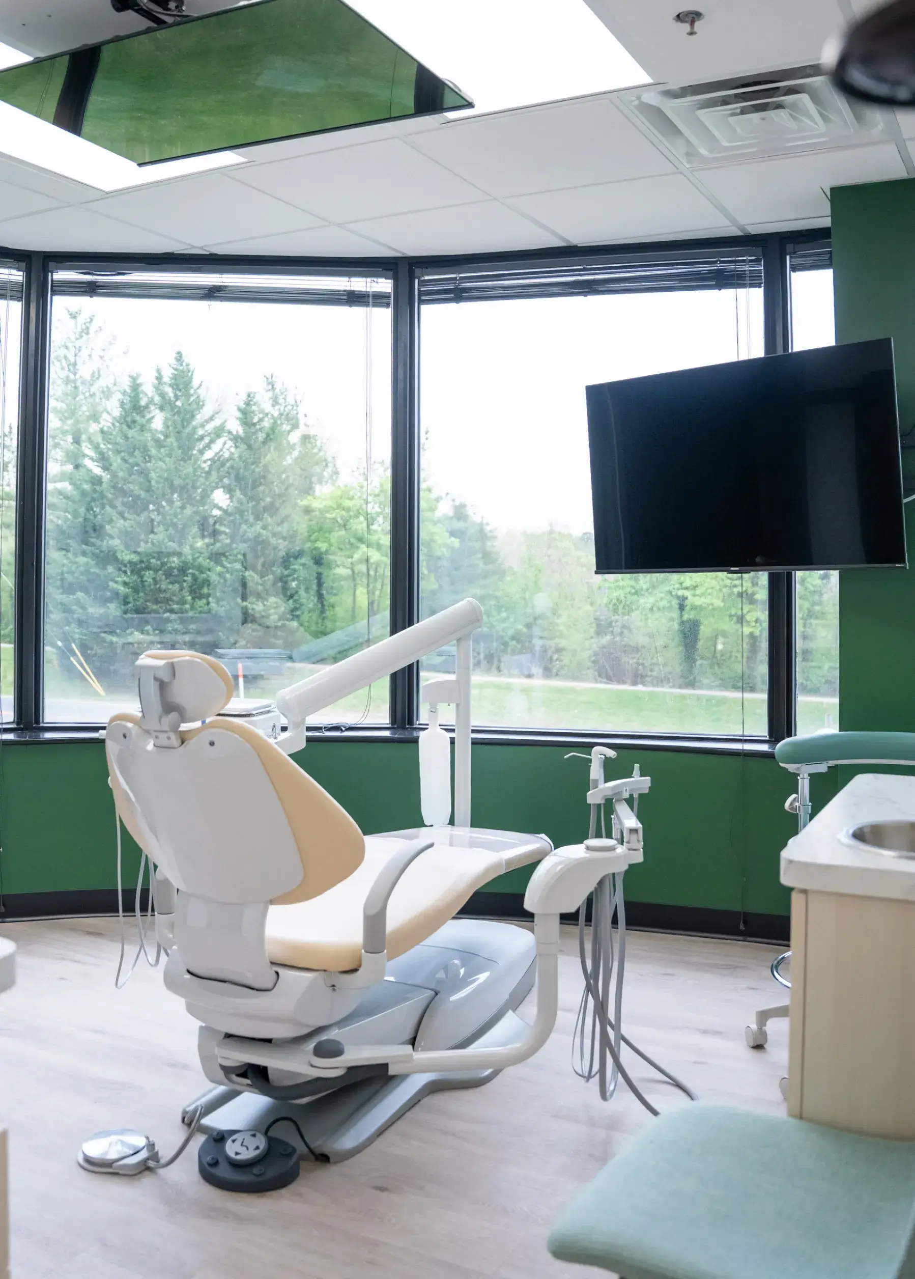 Dental examination chair in a modern clinic room with a large window and television.