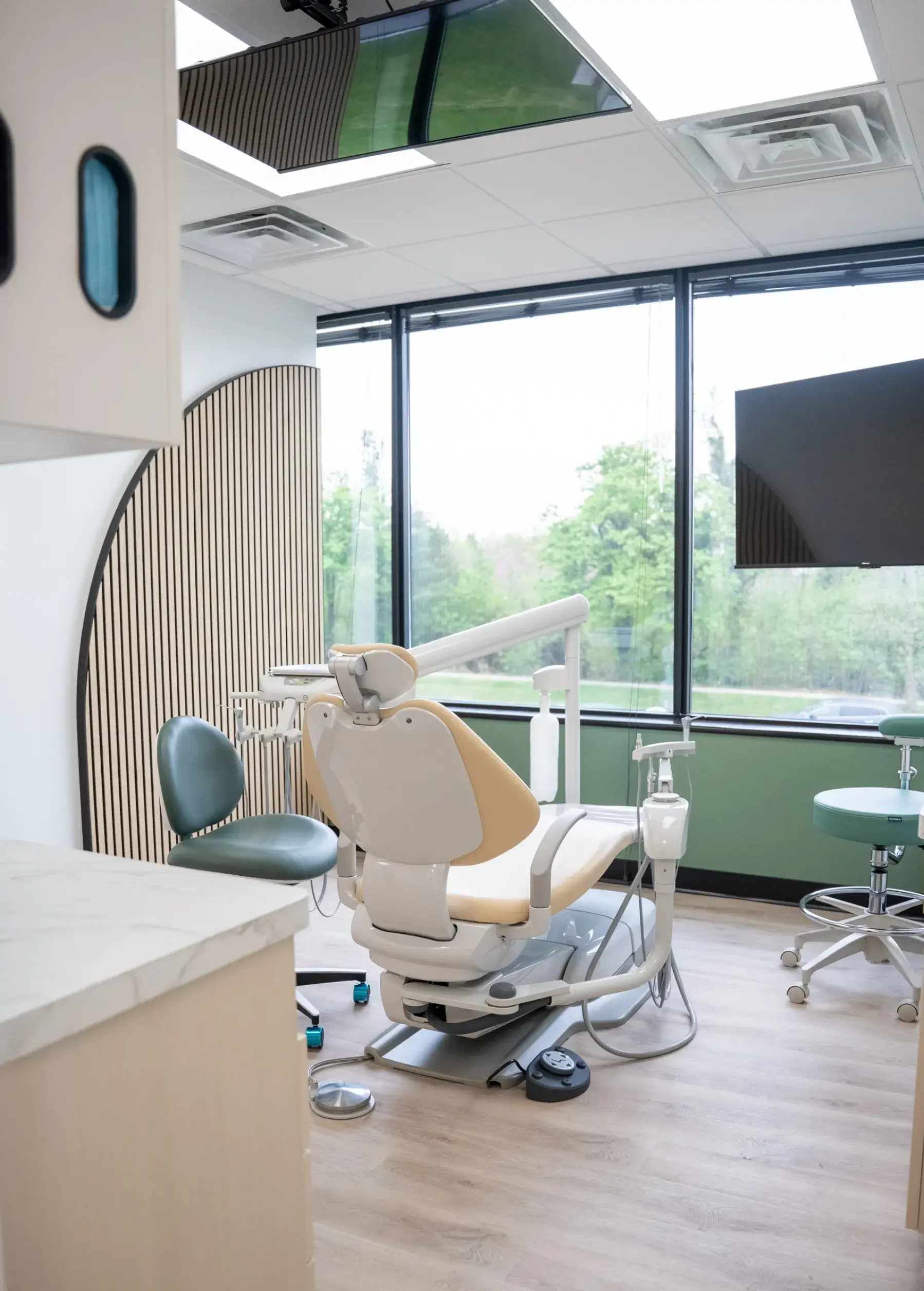 Dental examination room with a reclining chair, dental tools, and large windows letting in natural light.