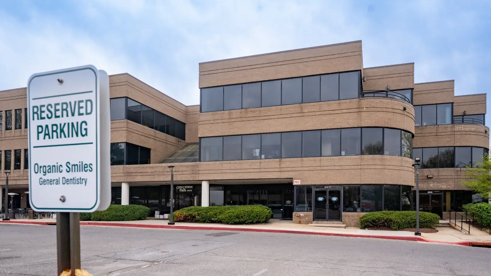Sign indicating reserved parking for Organic Smiles General Dentistry outside a large office building.