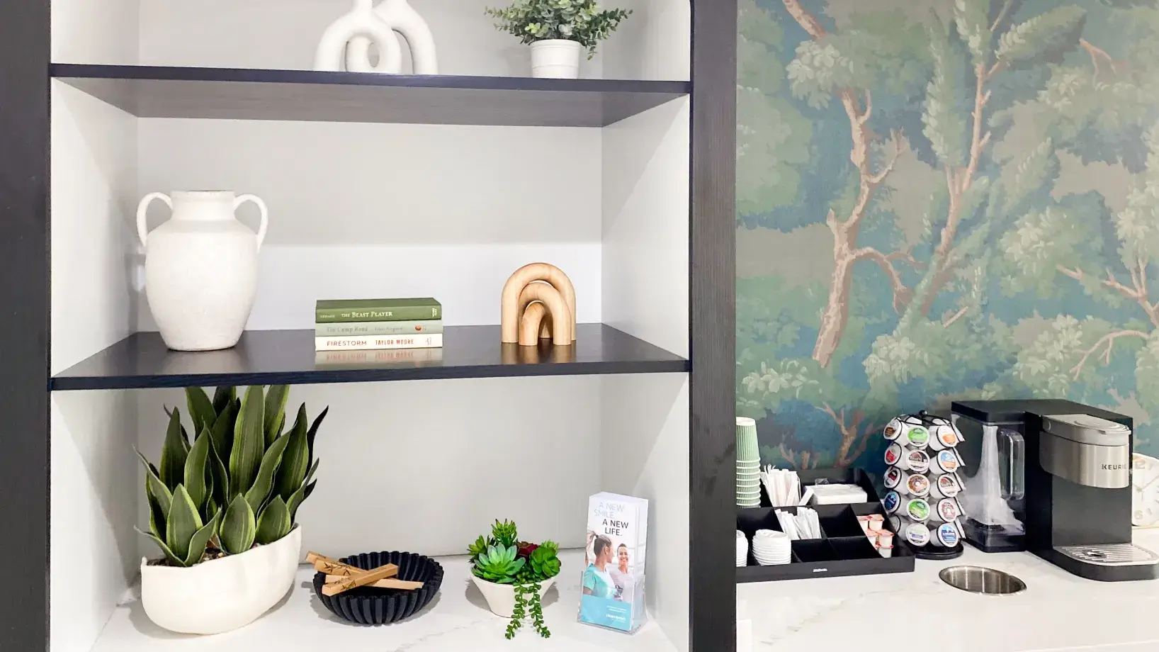 Books and decorative items on shelves next to a coffee station with pods and a machine.
