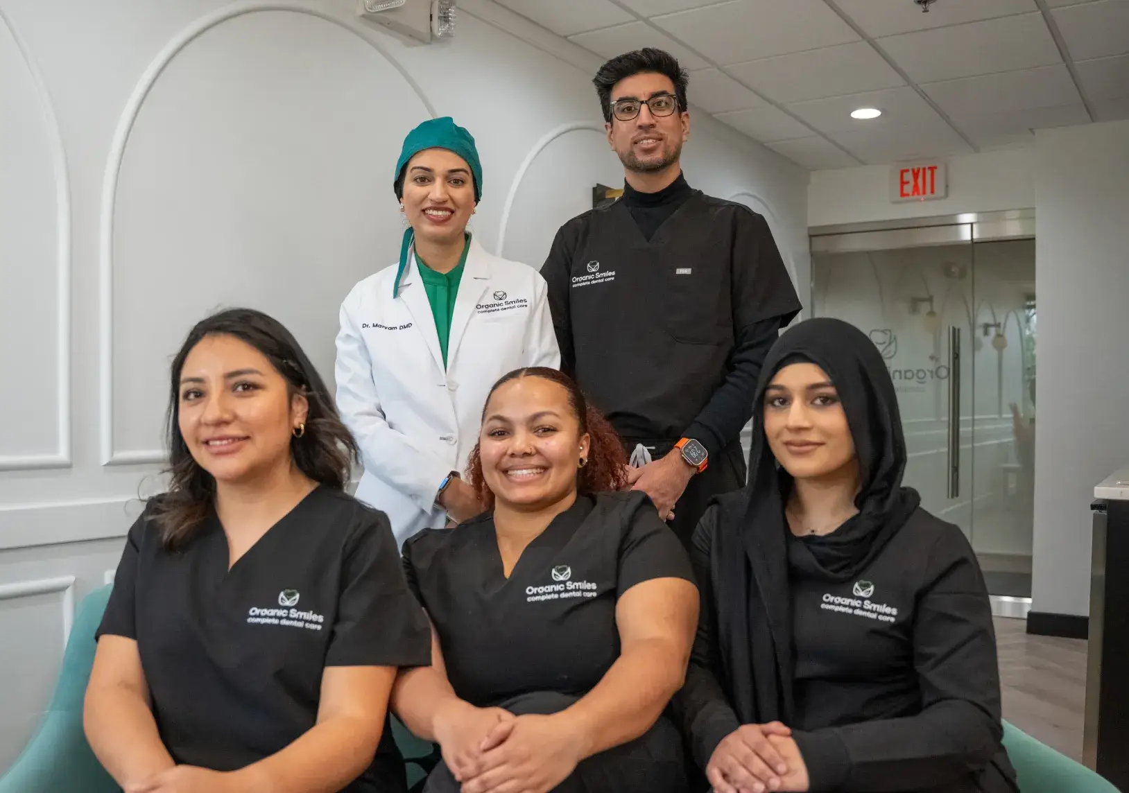 Five smiling healthcare professionals in uniforms pose together in a brightly lit office.