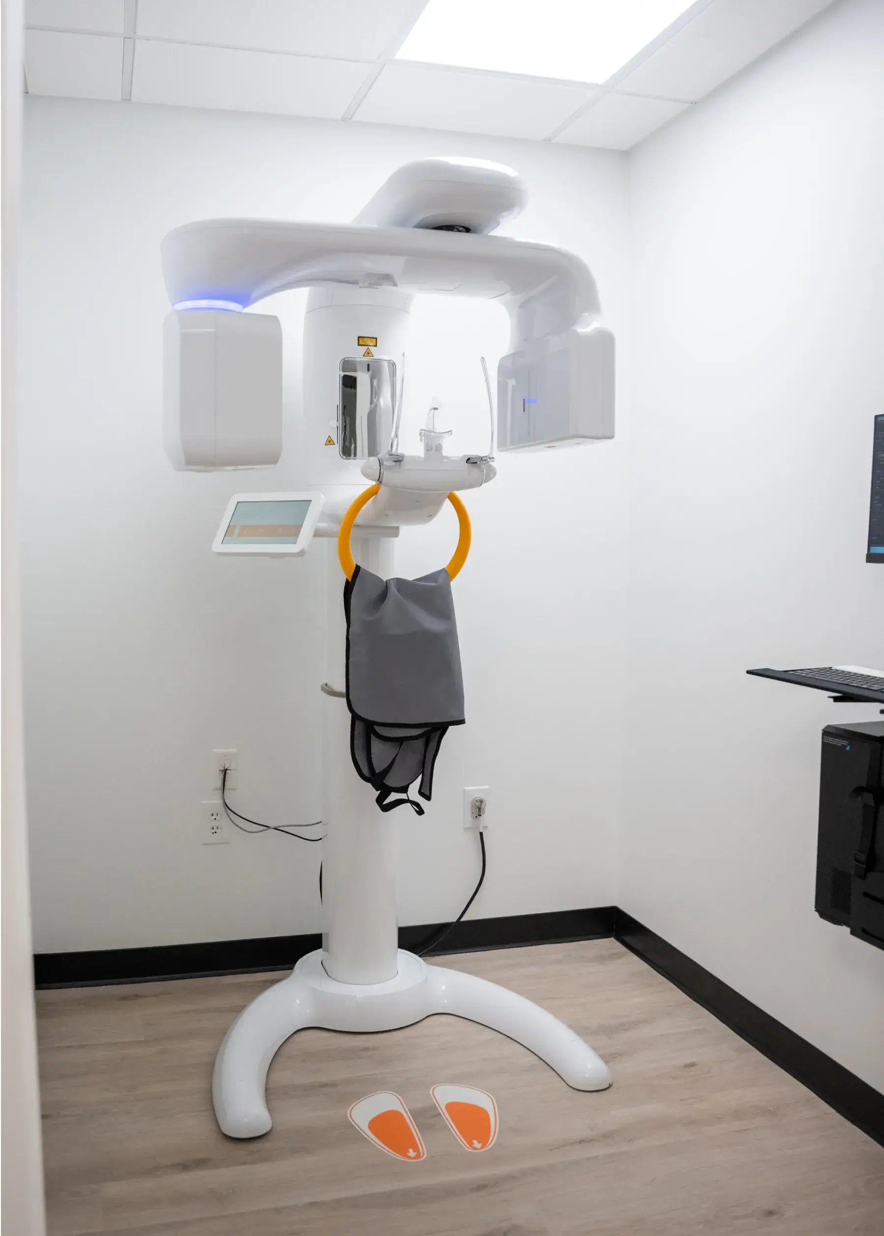 A dental X-ray machine stands in a room with a protective vest hanging in front.
