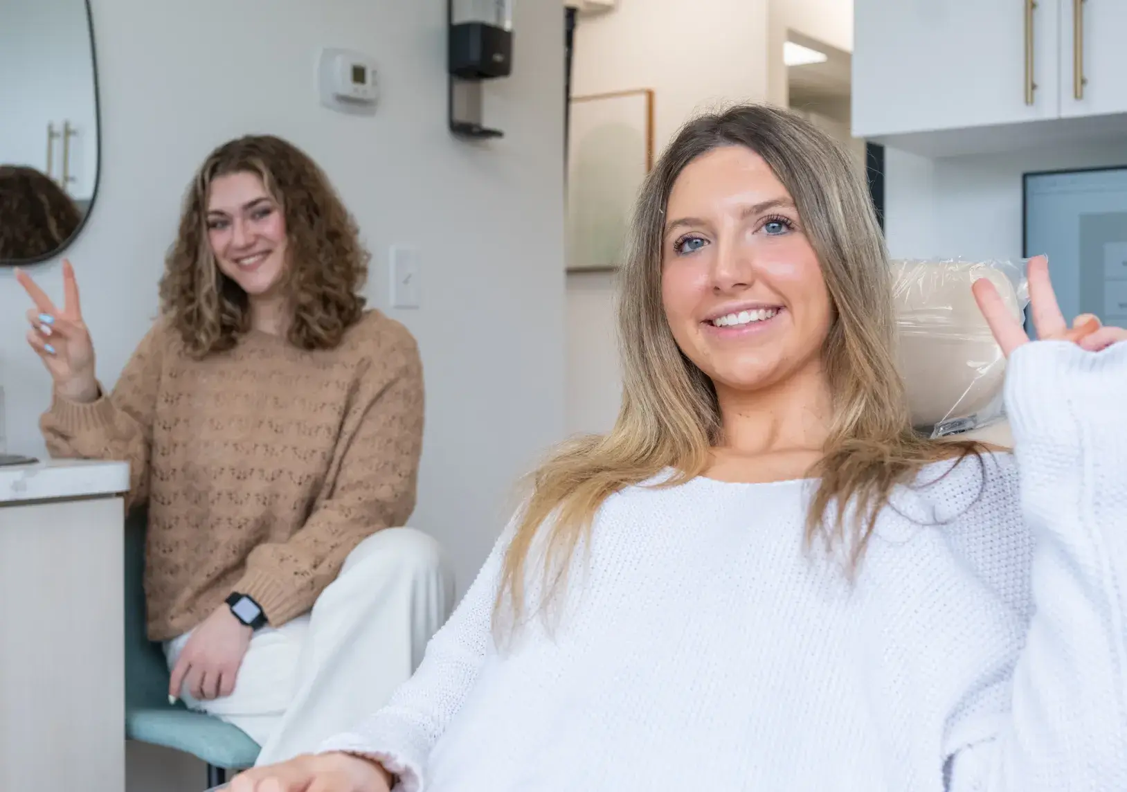 Two women indoors smiling and flashing peace signs at the camera.