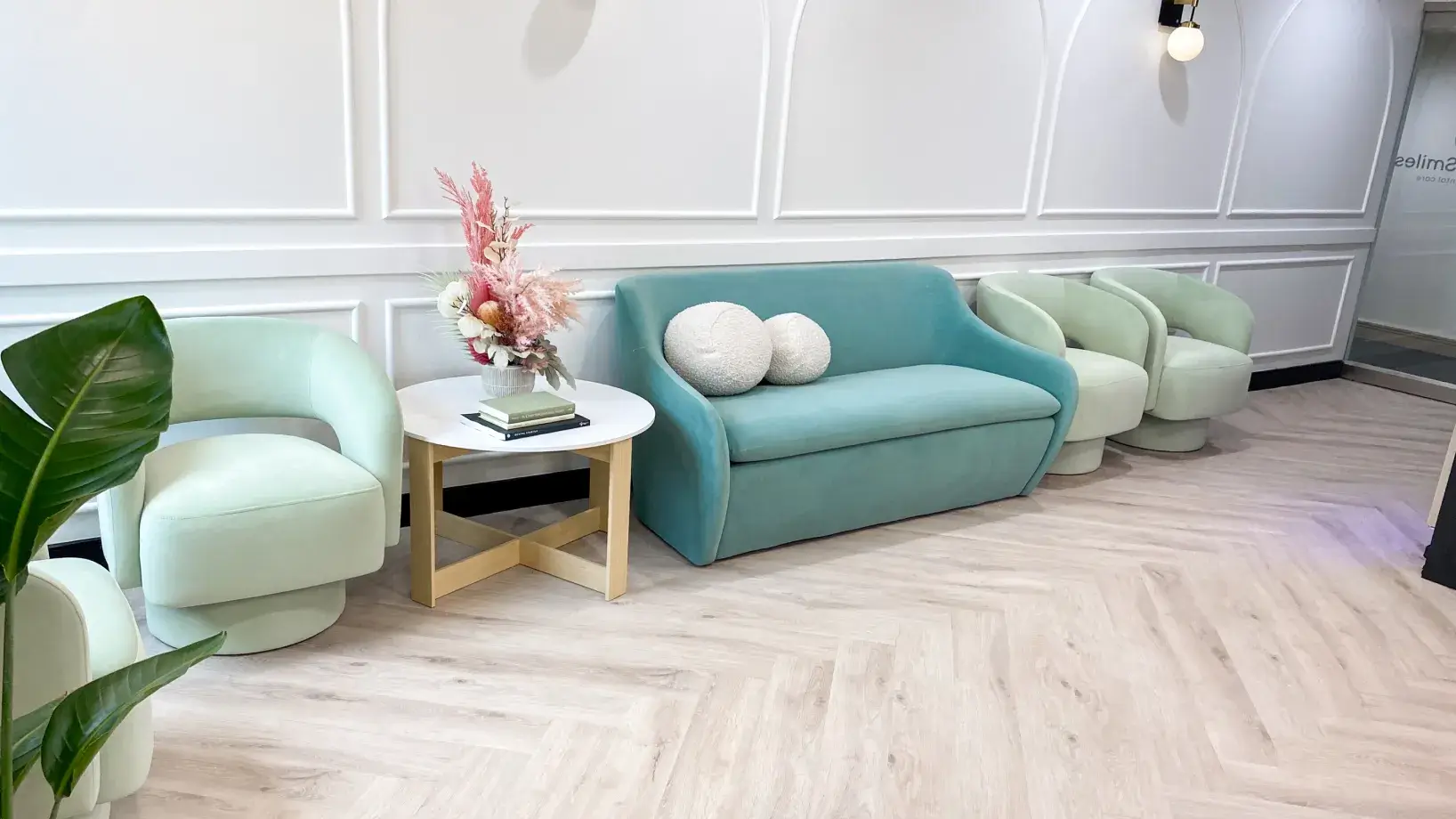 A modern waiting area with pastel chairs, a teal sofa, and a round table with a flower arrangement.