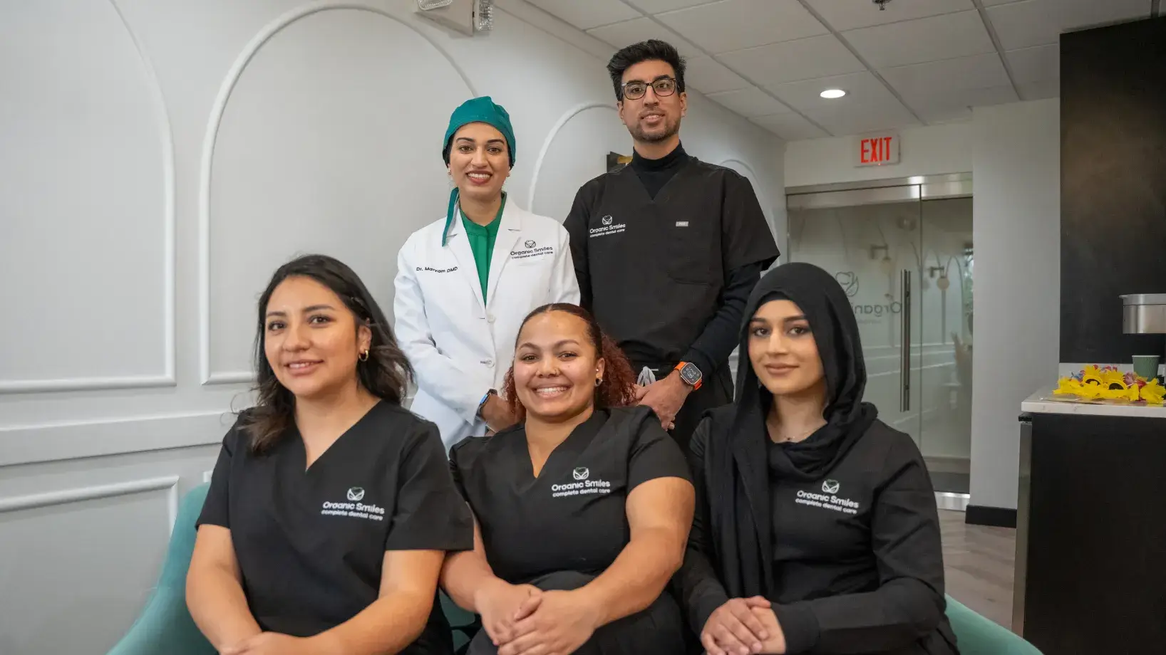 Five team members in dental scrubs pose together in a professional office setting.
