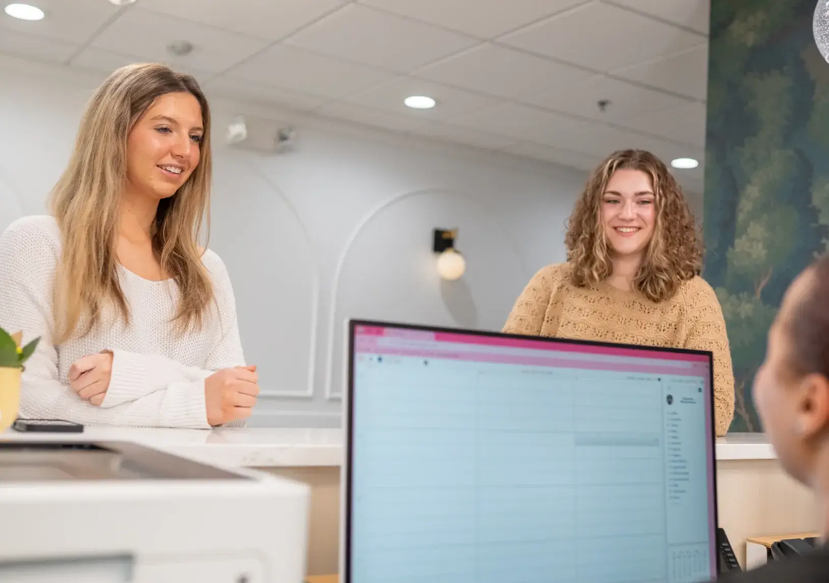 Two women standing at a counter, talking to a person seated at a computer.