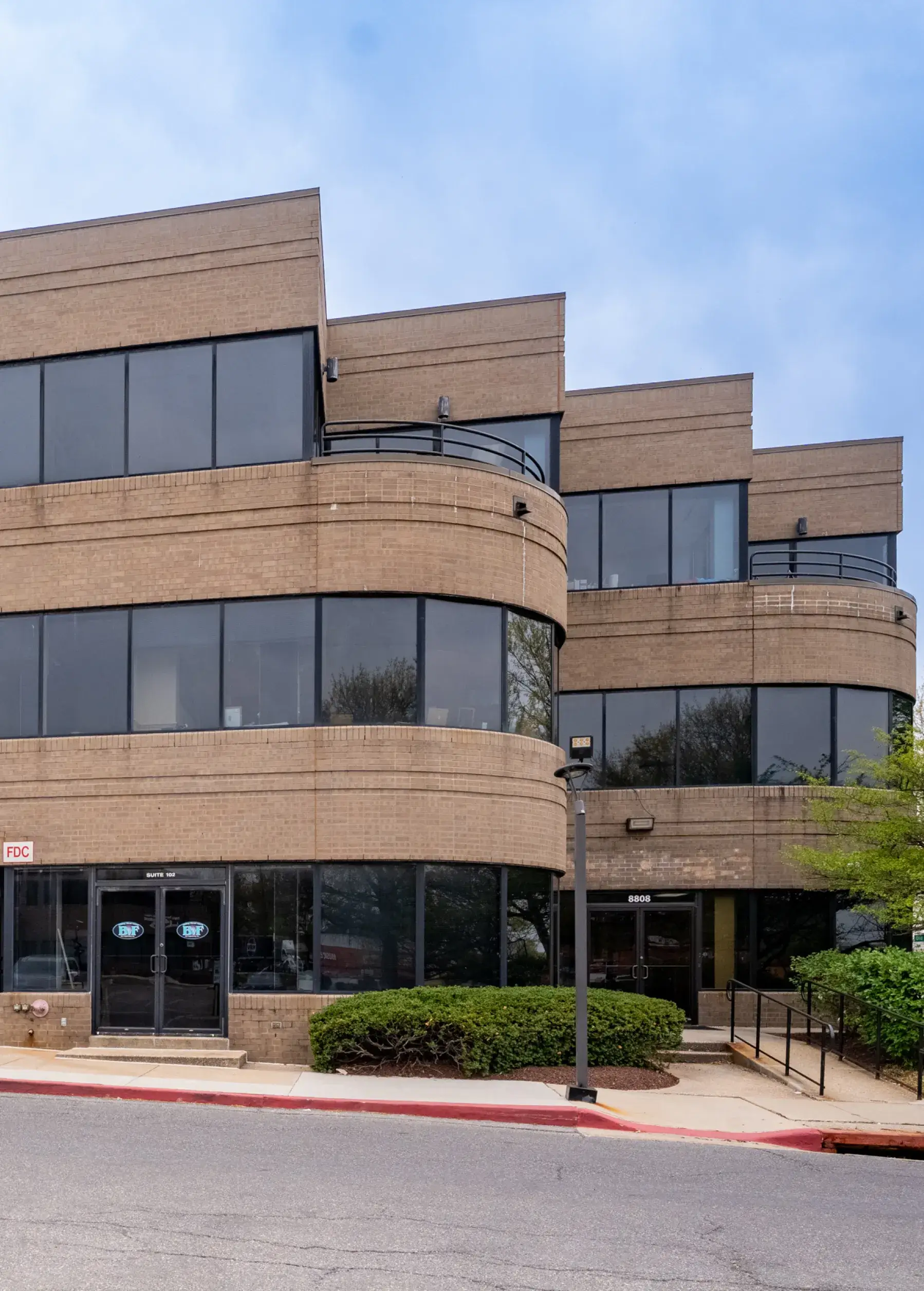 Three-story modern office building with large tinted windows and brick exterior under a blue sky.