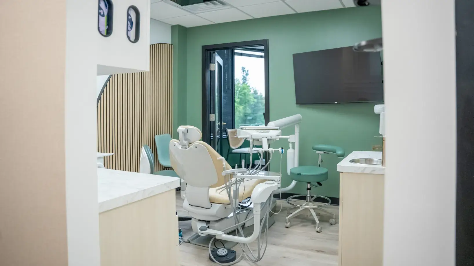 Dental office with a patient chair, dental equipment, and a wall-mounted screen.
