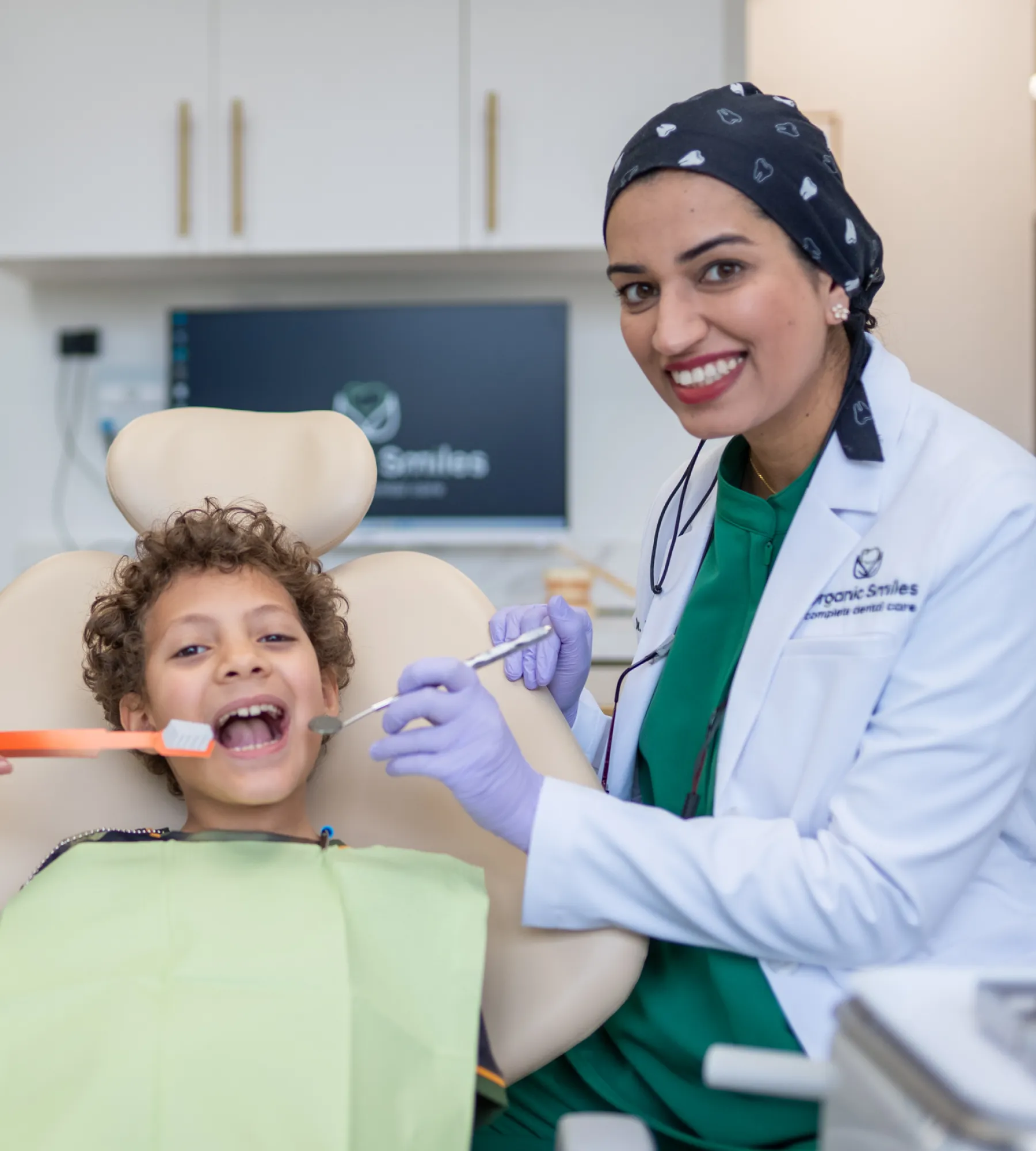 A dentist smiles while examining a child's teeth; both appear happy and relaxed.