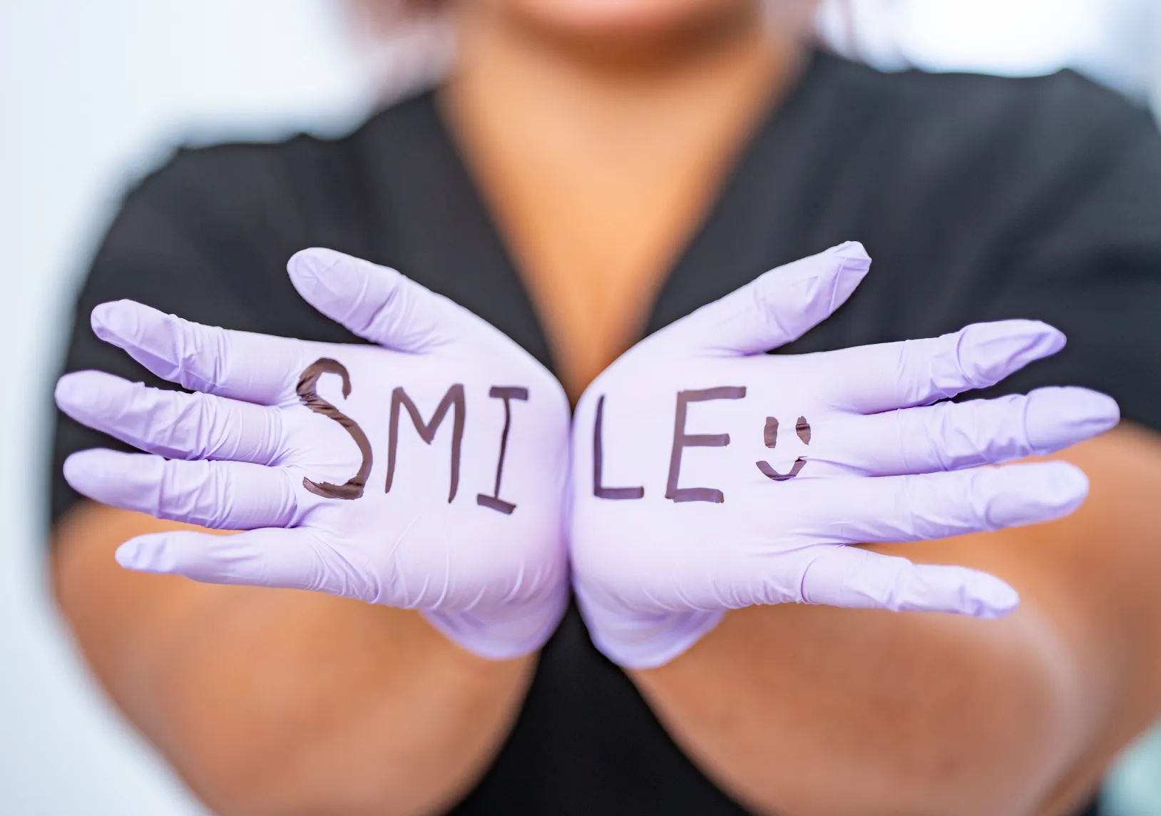 A person wearing purple gloves with "SMILE" written on them holds hands together facing forward.