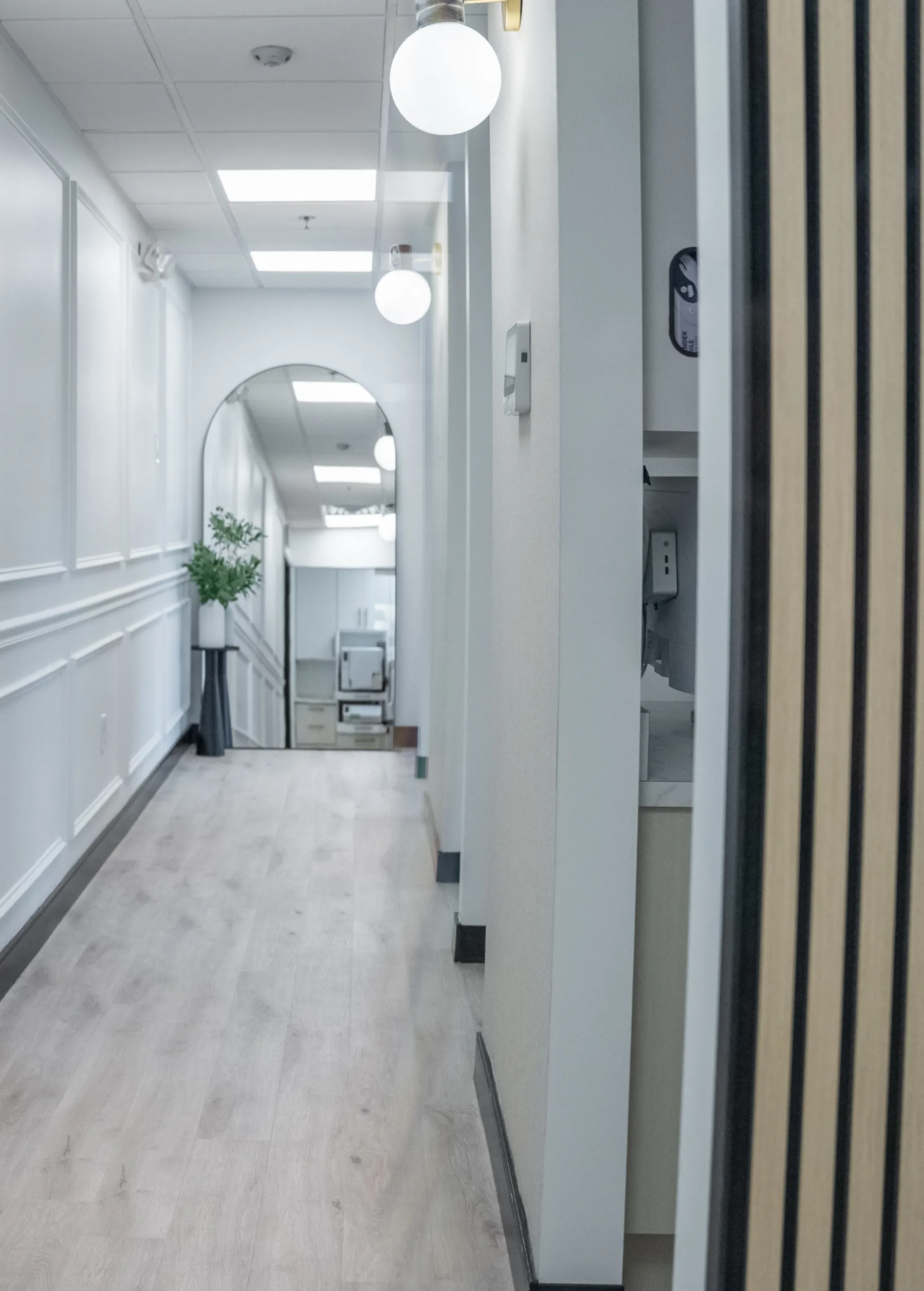 A long hallway with wooden flooring and round ceiling lights, featuring an archway at the end.