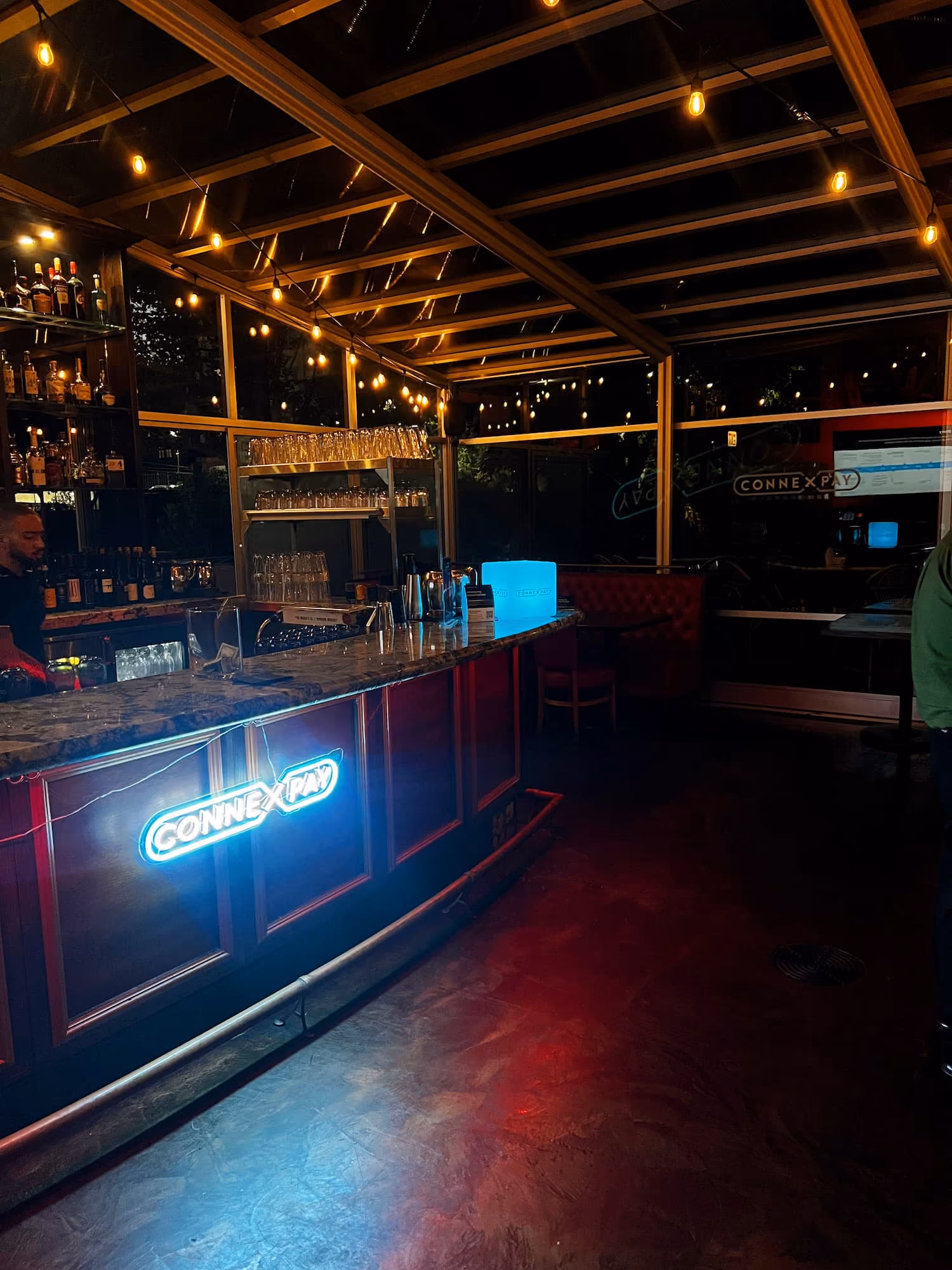 Dimly lit bar interior with a neon ConnexPay sign on the counter and string lights on the ceiling.
