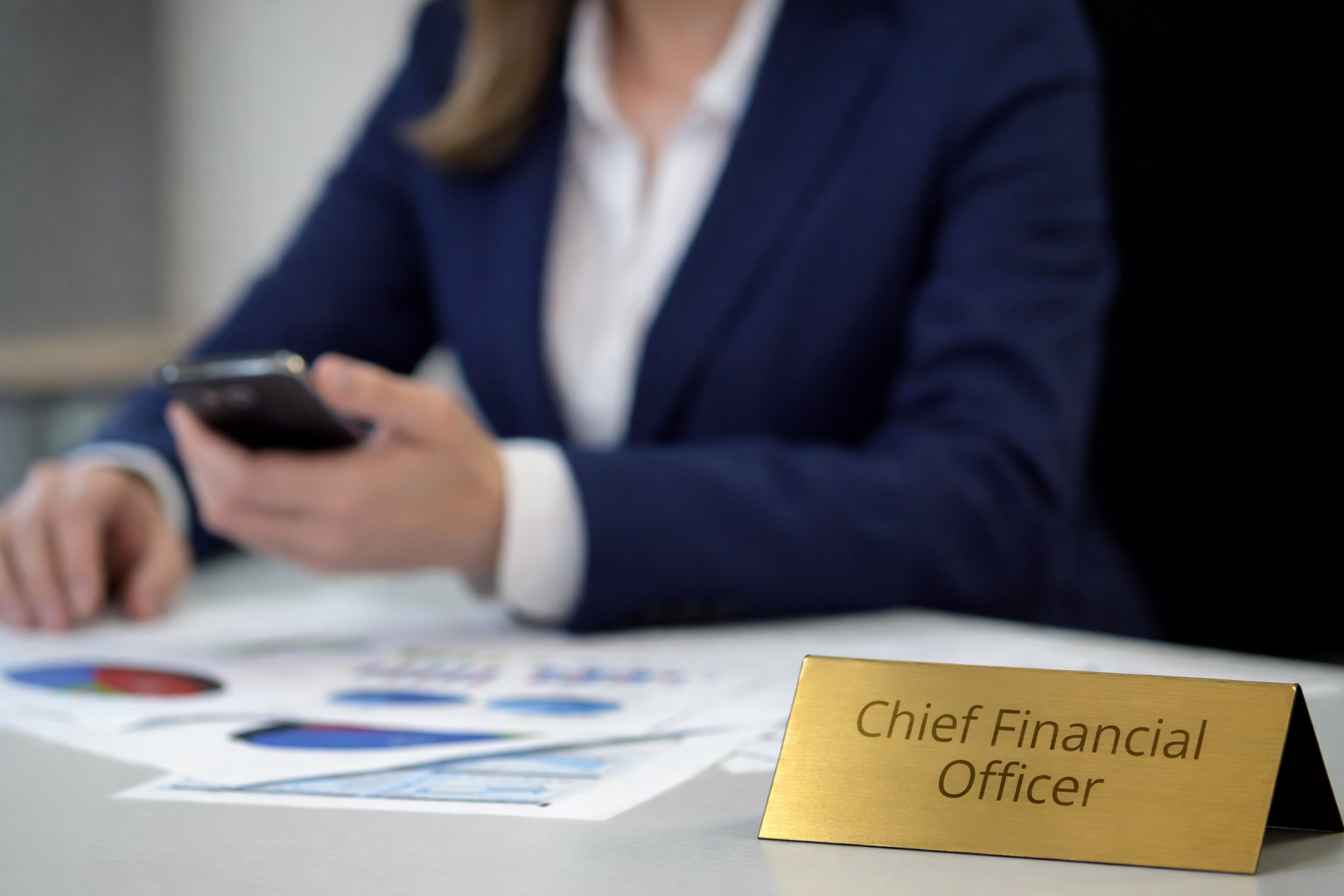 Chief Financial Officer nameplate on desk with professional reviewing documents in background