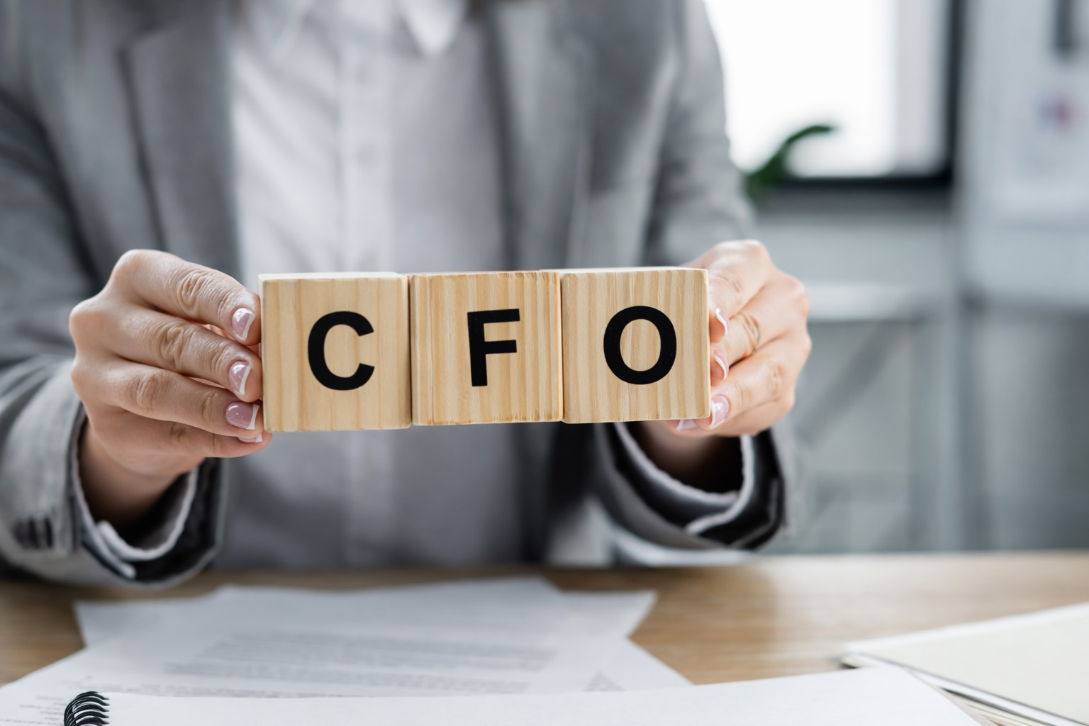 Professional holding wooden blocks spelling "CFO" over paperwork at a desk