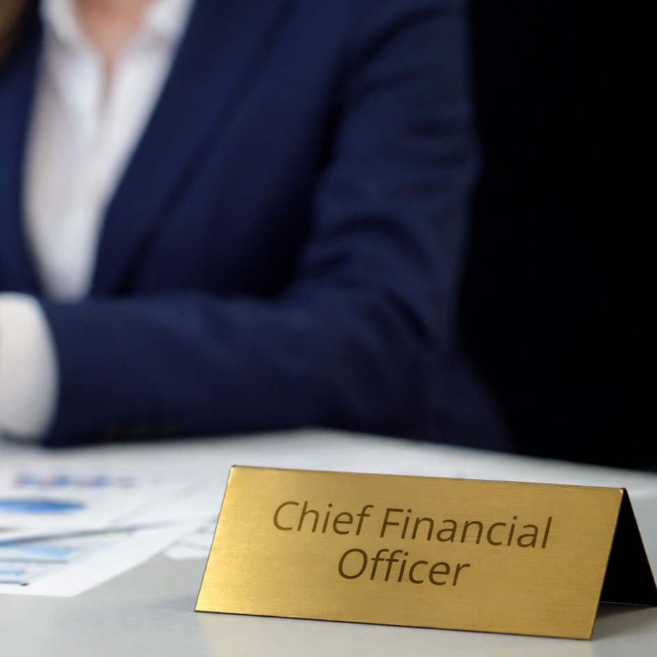 Chief Financial Officer nameplate on desk with professional reviewing documents in background