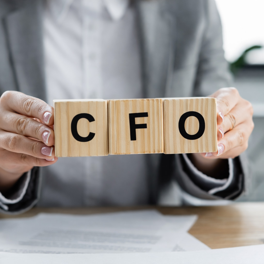 Professional holding wooden blocks spelling "CFO" over paperwork at a desk