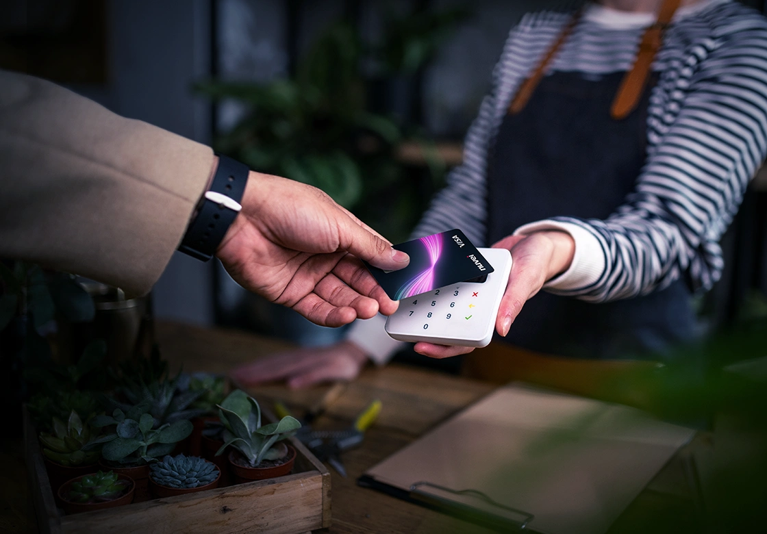 An image of two people in a payment transaction: one behind the counter and the client using contactless technology. 