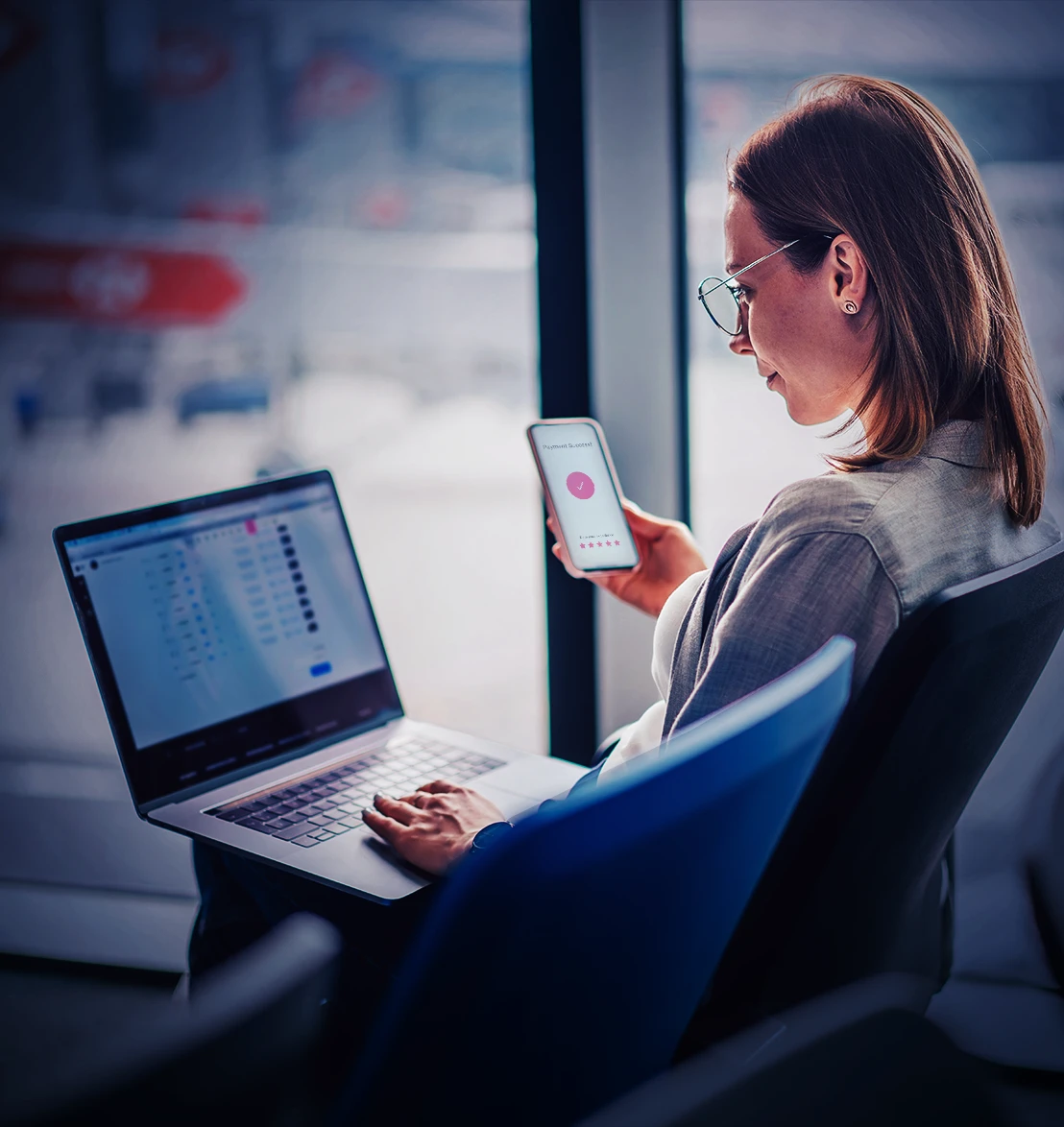 A woman sitting with her laptop and her cellphone checking her payouts.