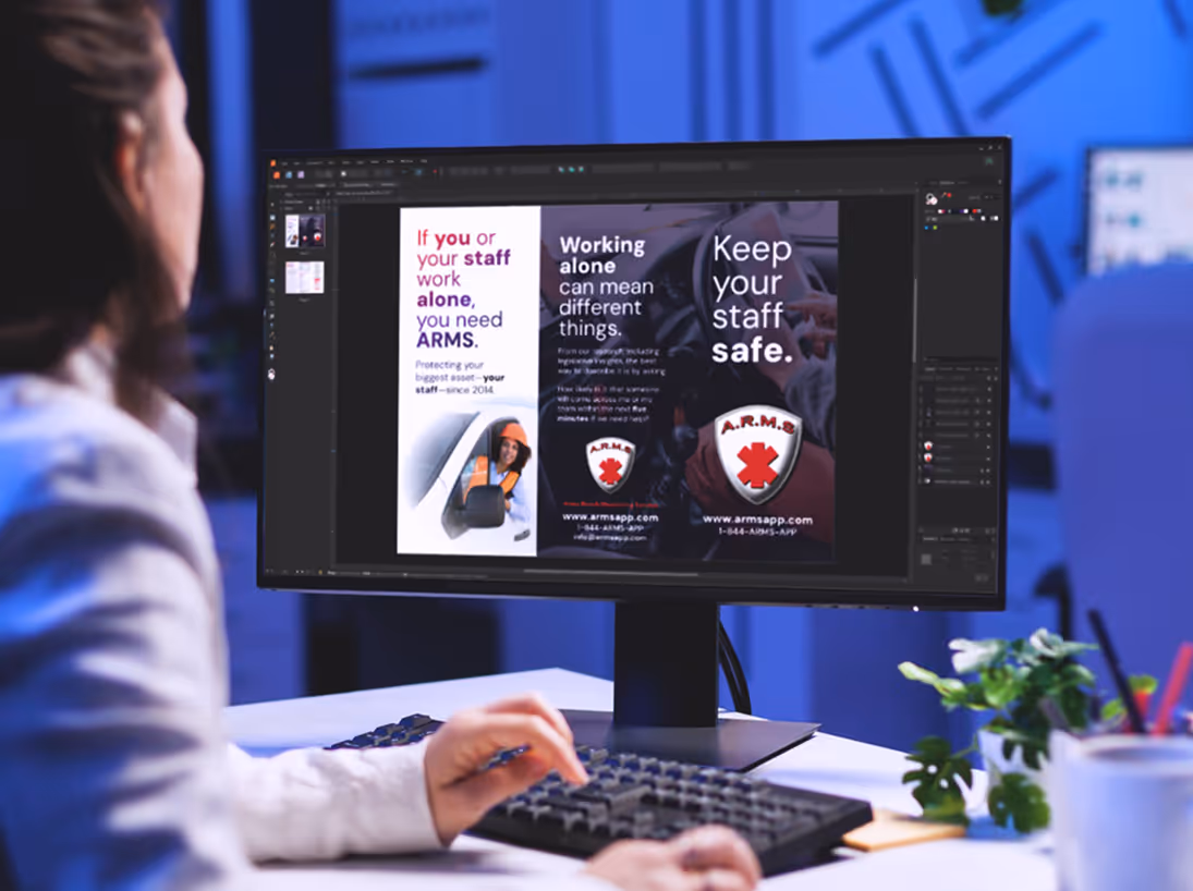 A person sitting at a desk with a computer displaying graphic design work.