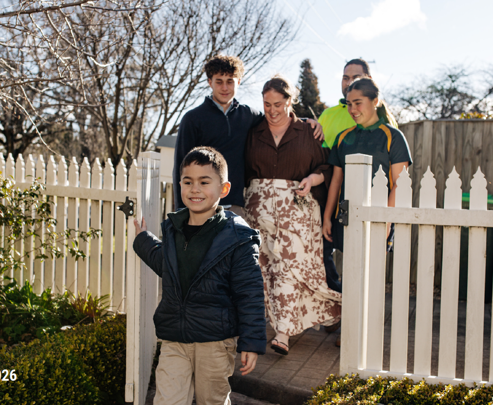 Young boy enters the front gate of a home with his parents, brother and sister behind him.