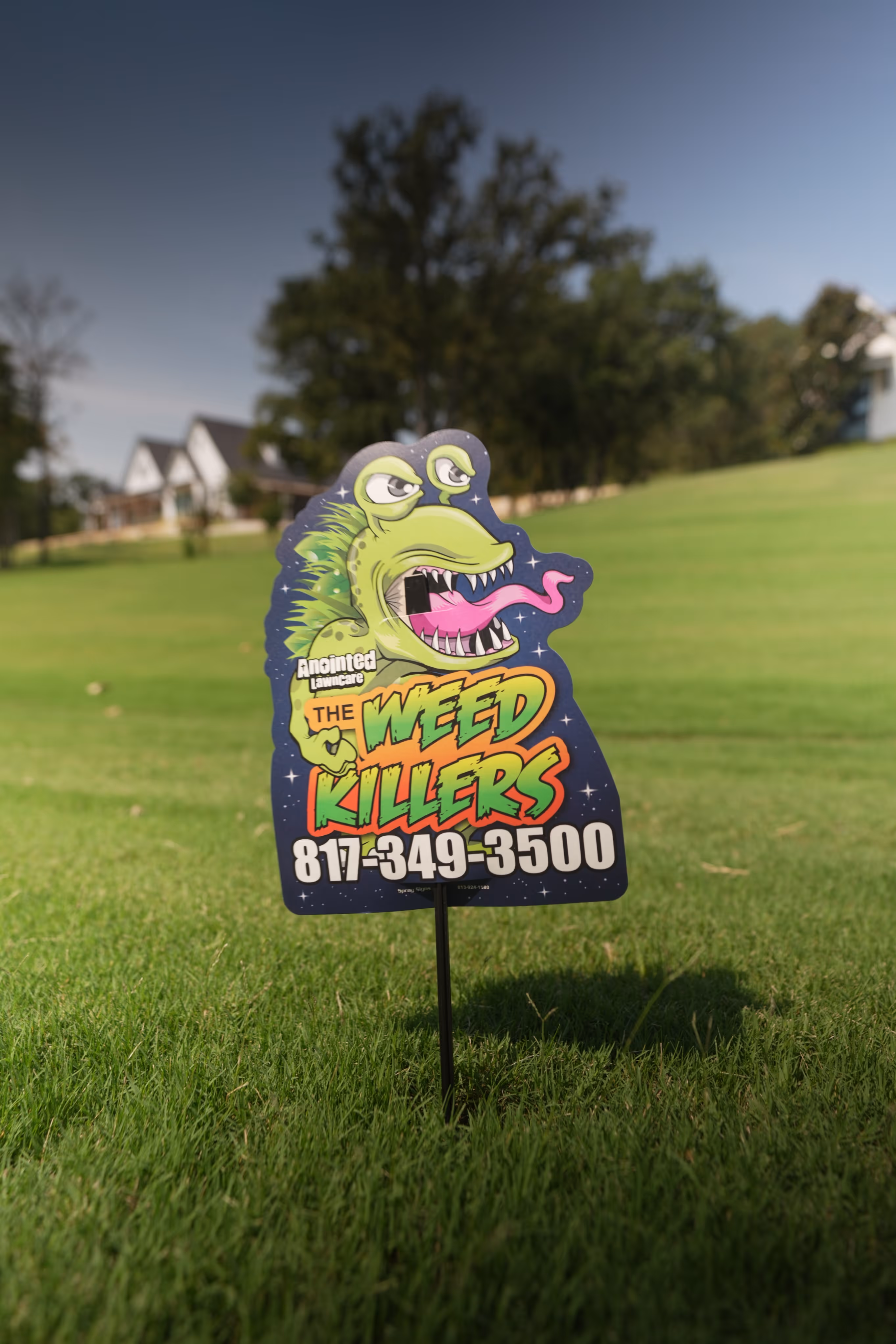 Lawn sign with a green monster illustration and text advertising The Weed Killers