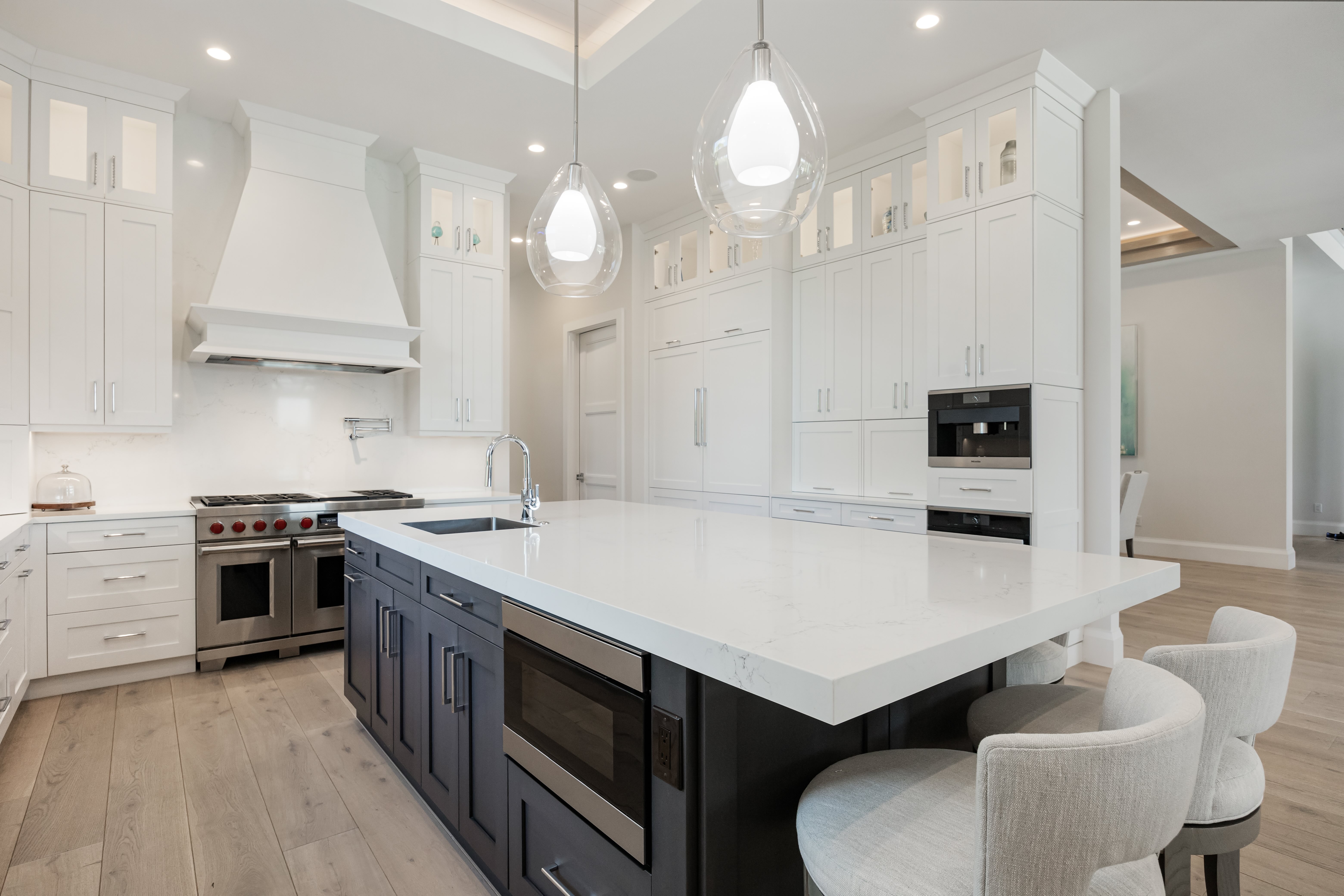 Modern kitchen with large white marble island, dark cabinets, stainless steel appliances, and white cabinetry.
