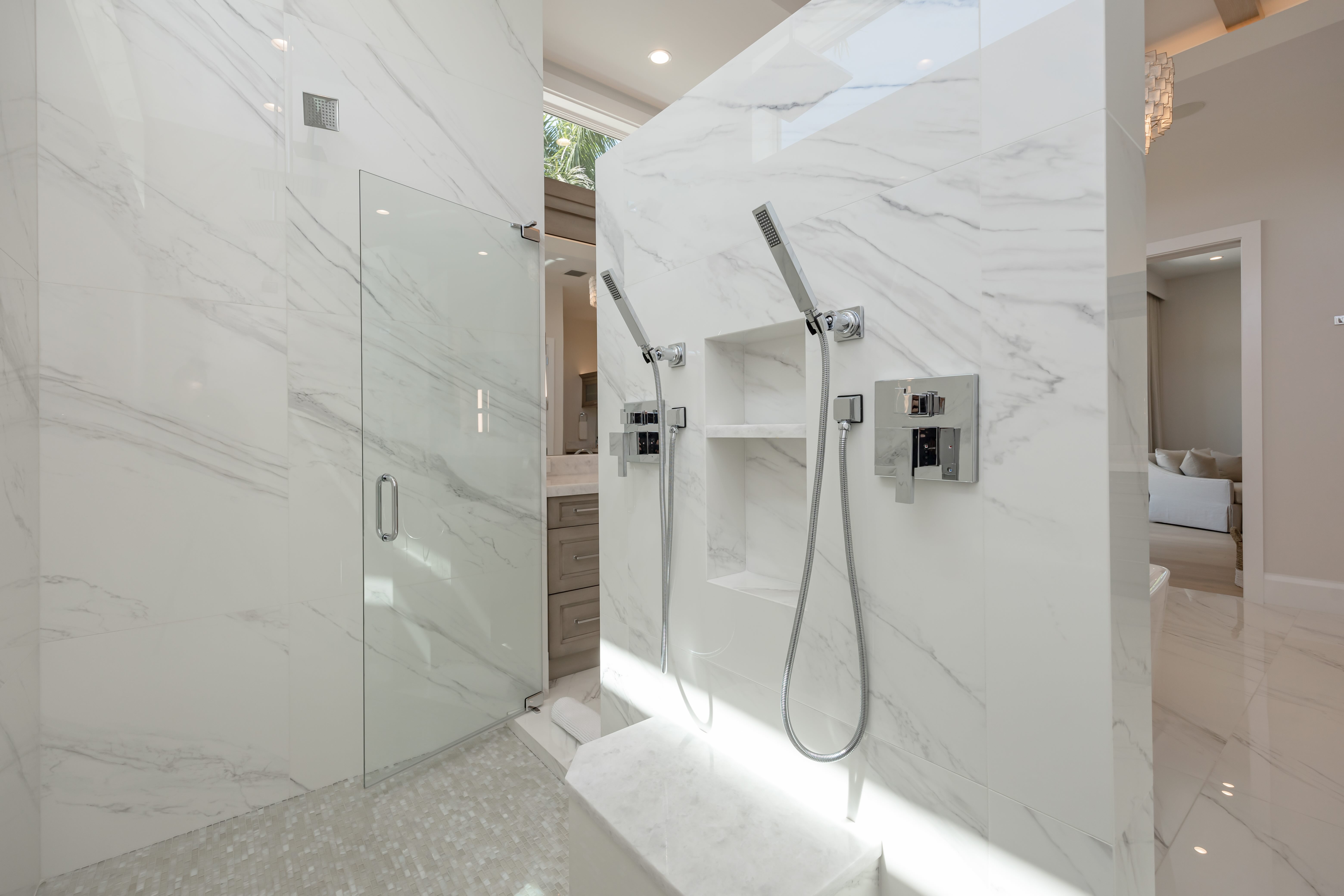 Modern bathroom shower with white marble walls, dual handheld showerheads, and a glass door.
