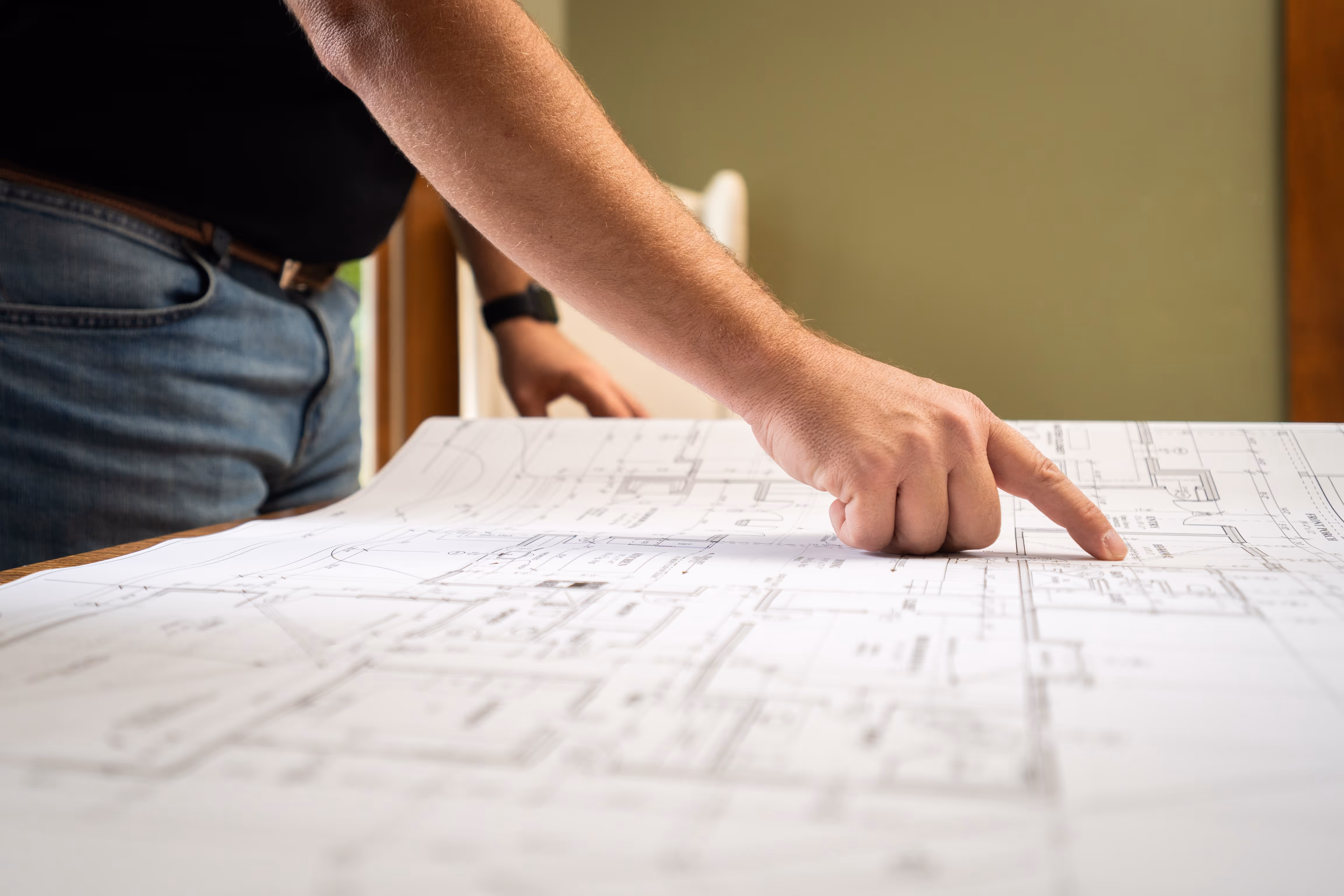 Person pointing at a blueprint or architectural plan on a table.