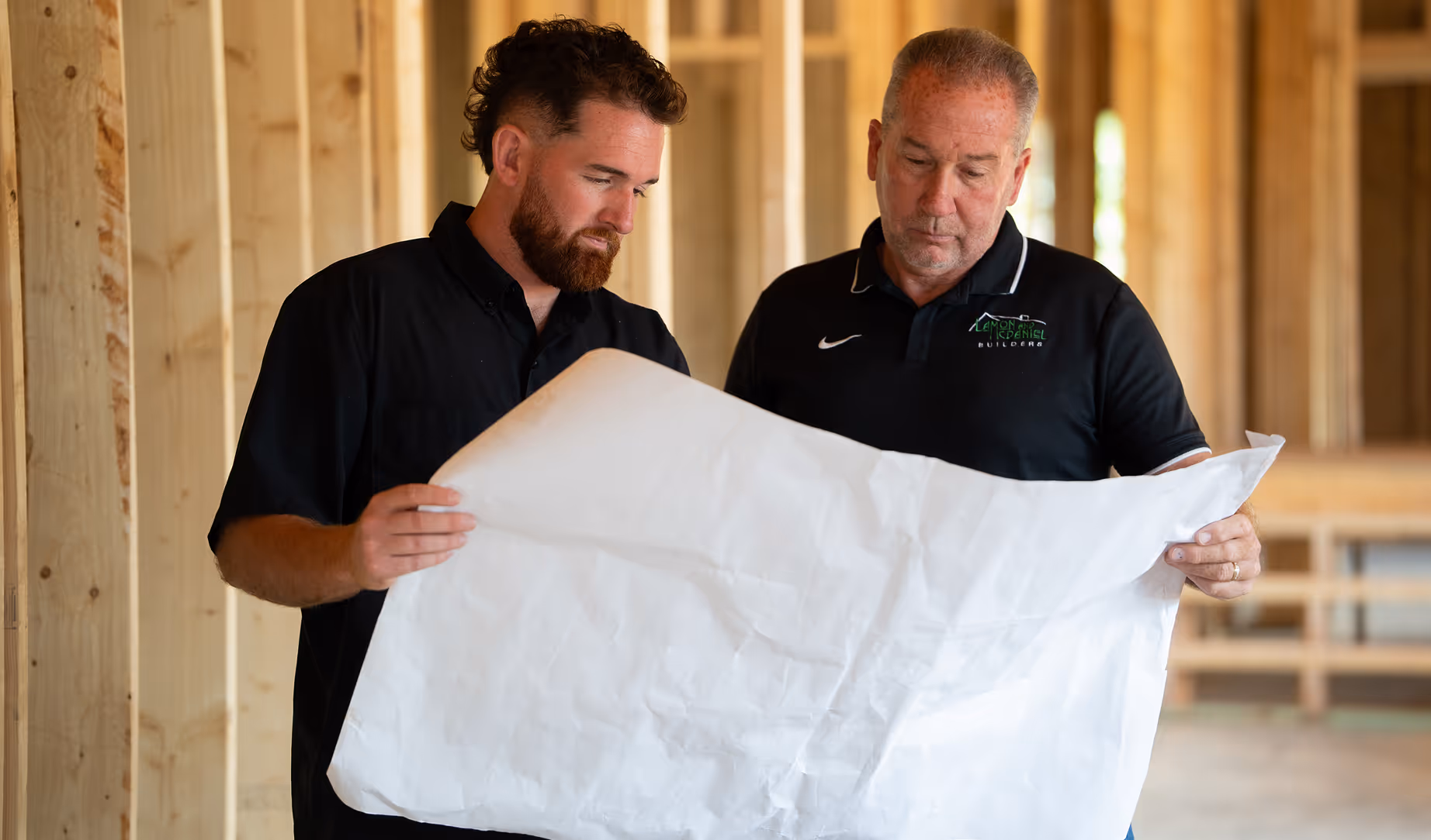 Two men in a wooden framed building reviewing large construction blueprints.