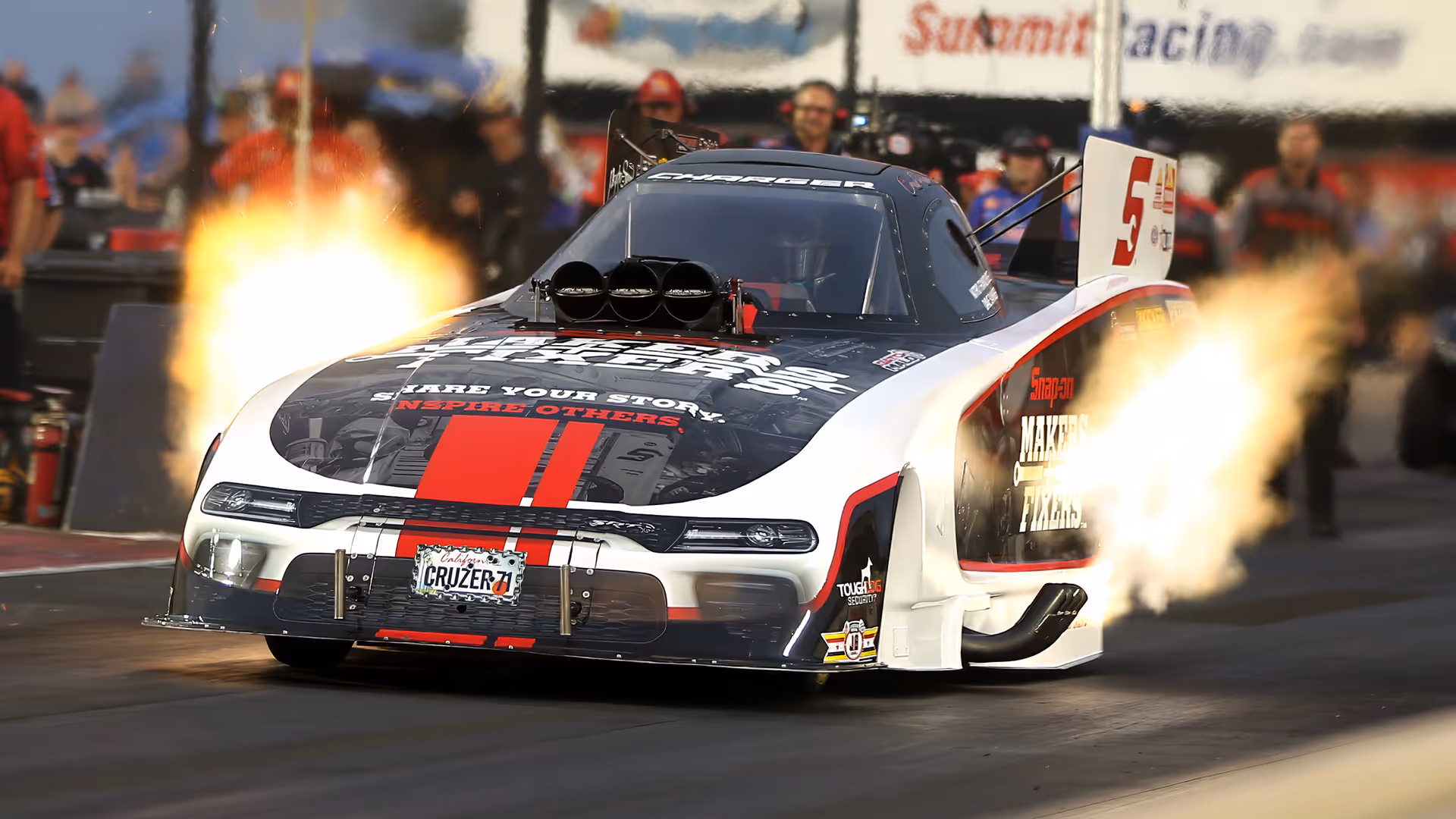 Drag racing car with flames bursting from exhaust pipes speeding down the race track.